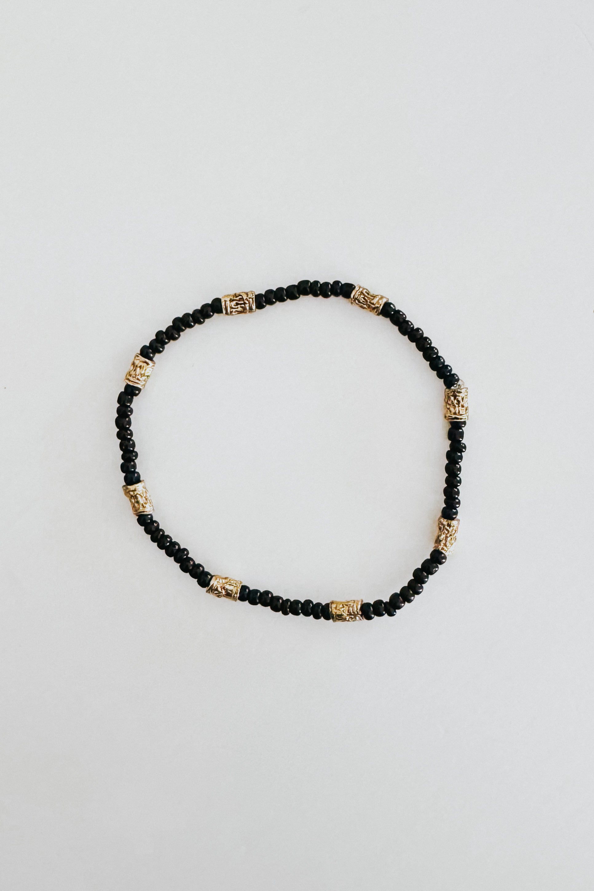 Delicate bracelet featuring small black beads interspersed with ornate gold-toned cylindrical accents on a light surface