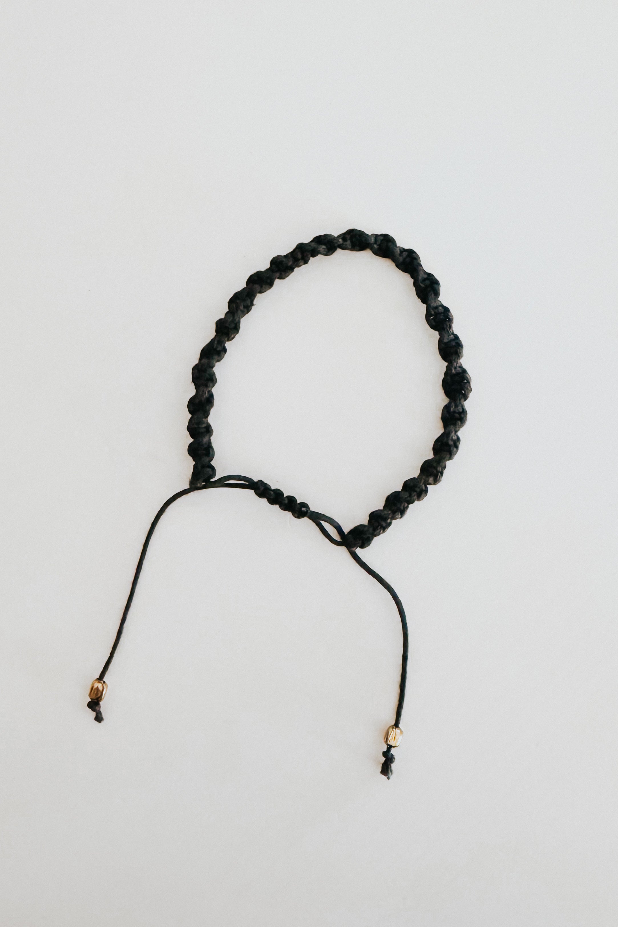 Black adjustable knotted bracelet with small gold bead accents displayed on a light background