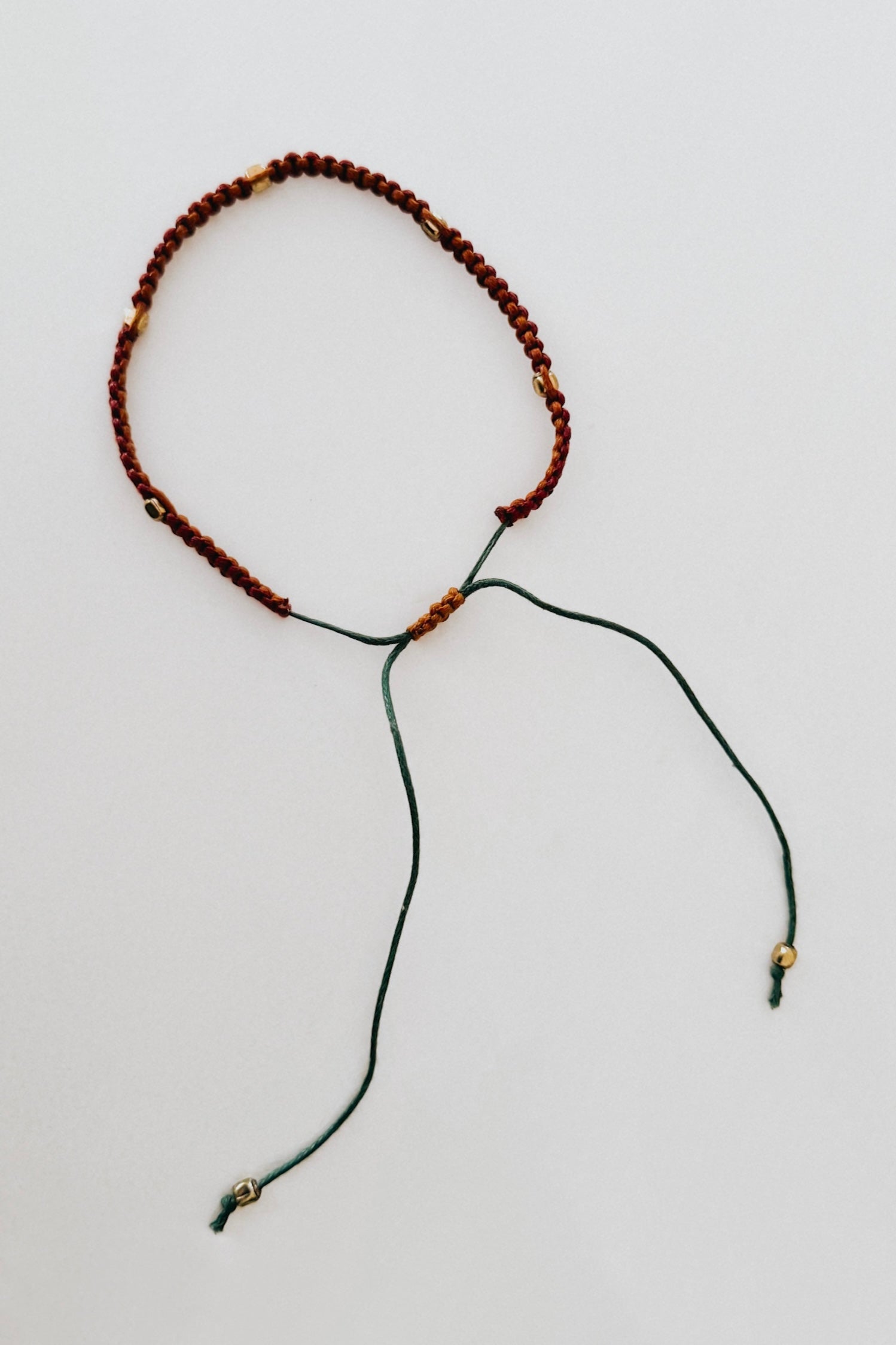 Adjustable brown woven bracelet with gold accents and green adjustable cord on a white background