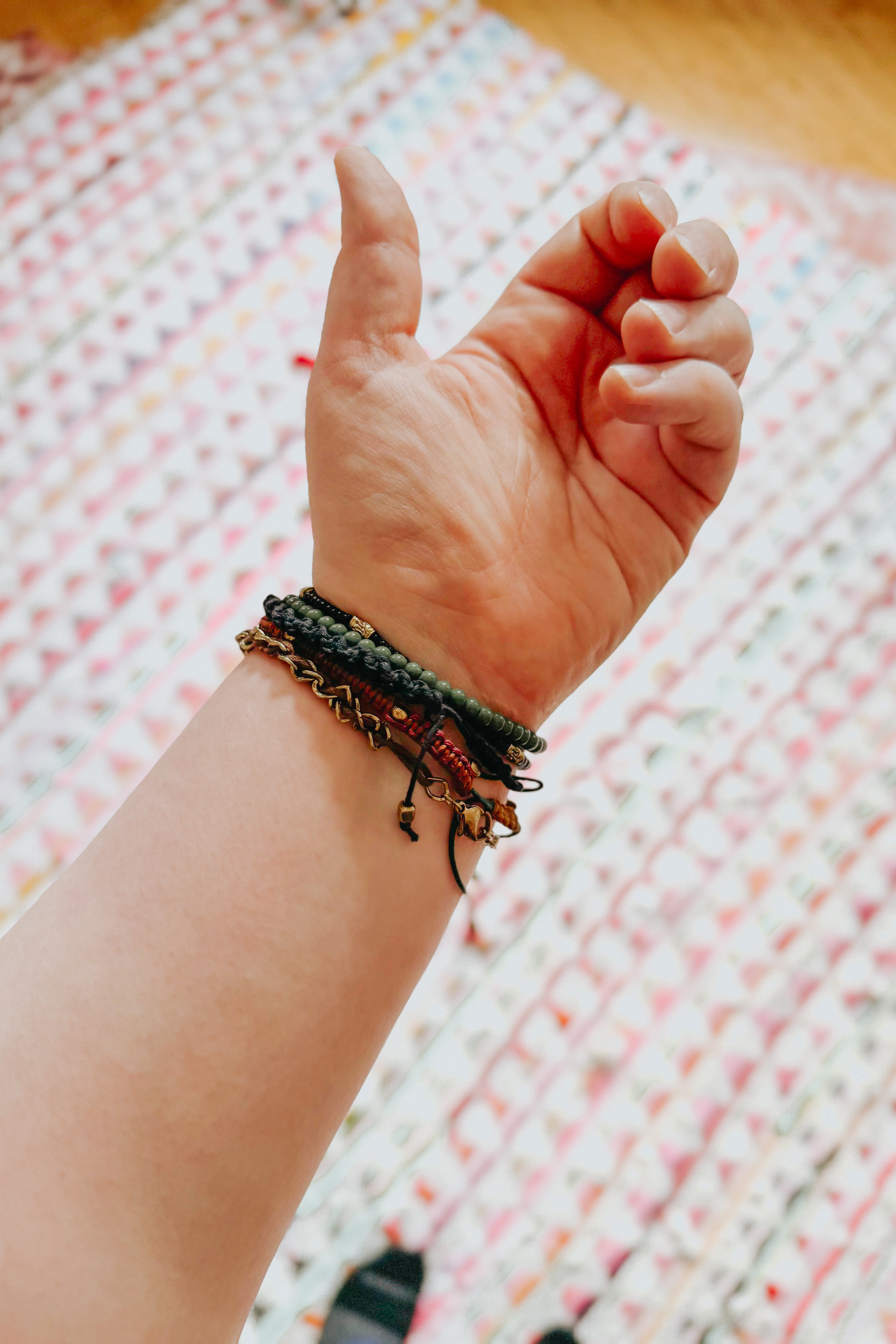 Wrist adorned with layered green and brown textured Ember Stackable bracelets over a patterned fabric background