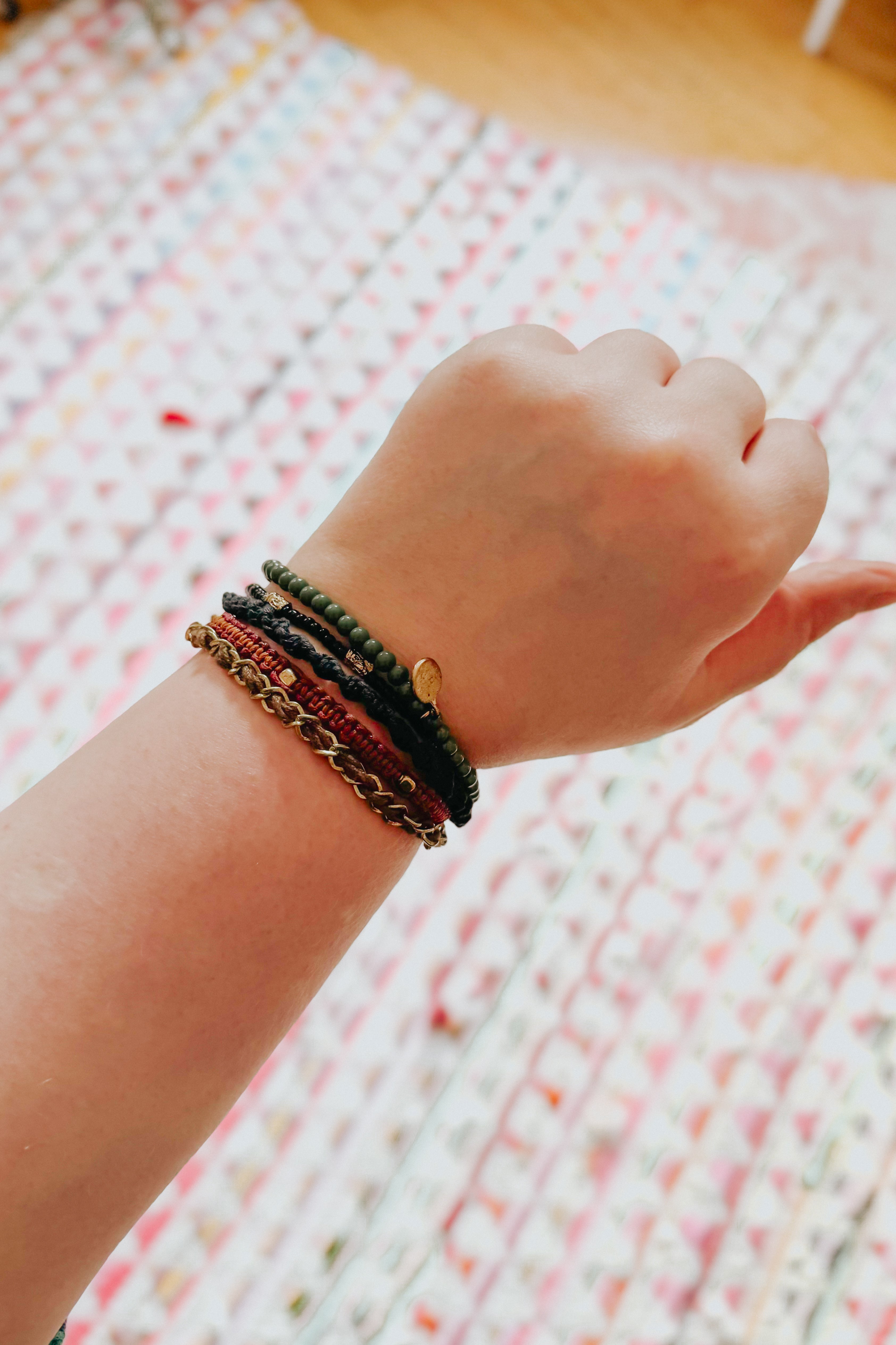 Close-up of wrist wearing a stack of earthy-toned Ember Stackable bracelets against patterned background