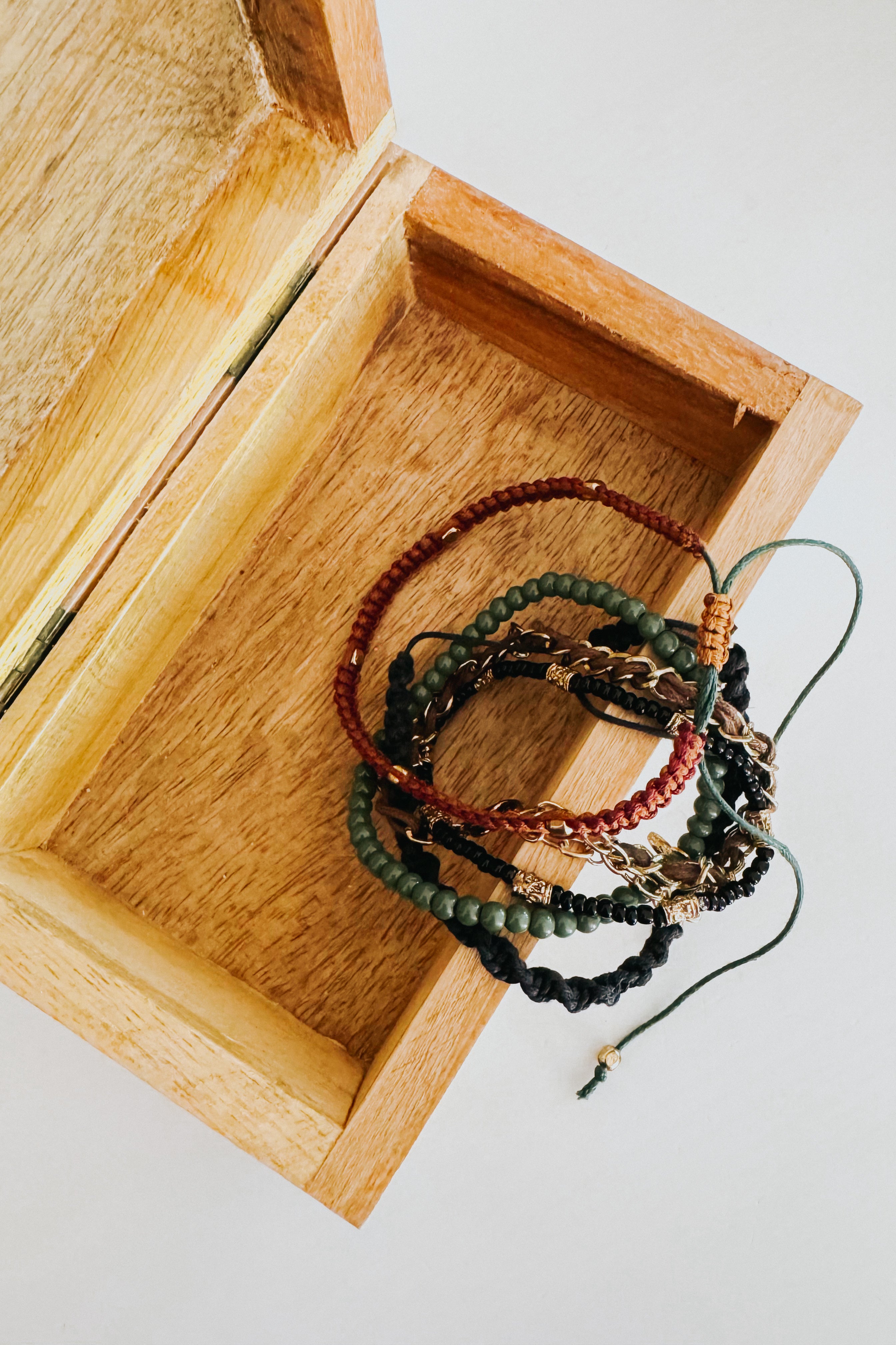 Ember Stackable Bracelet Set with braided cords, green beads, and gold details inside an open wooden box on white surface