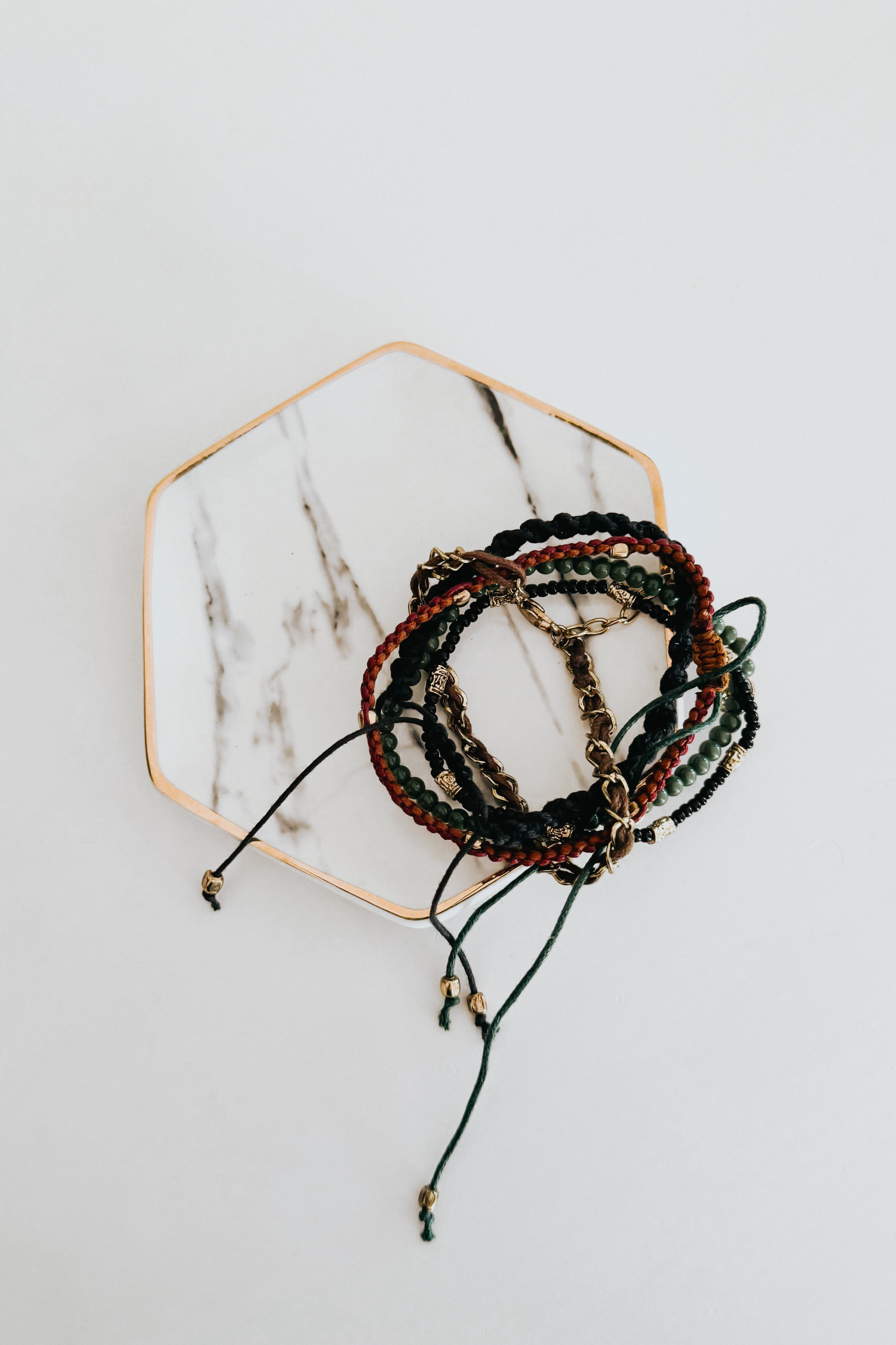 Entwined stackable Ember bracelets with braided cords, assorted beads, and gold-toned chains on marble hexagon tray