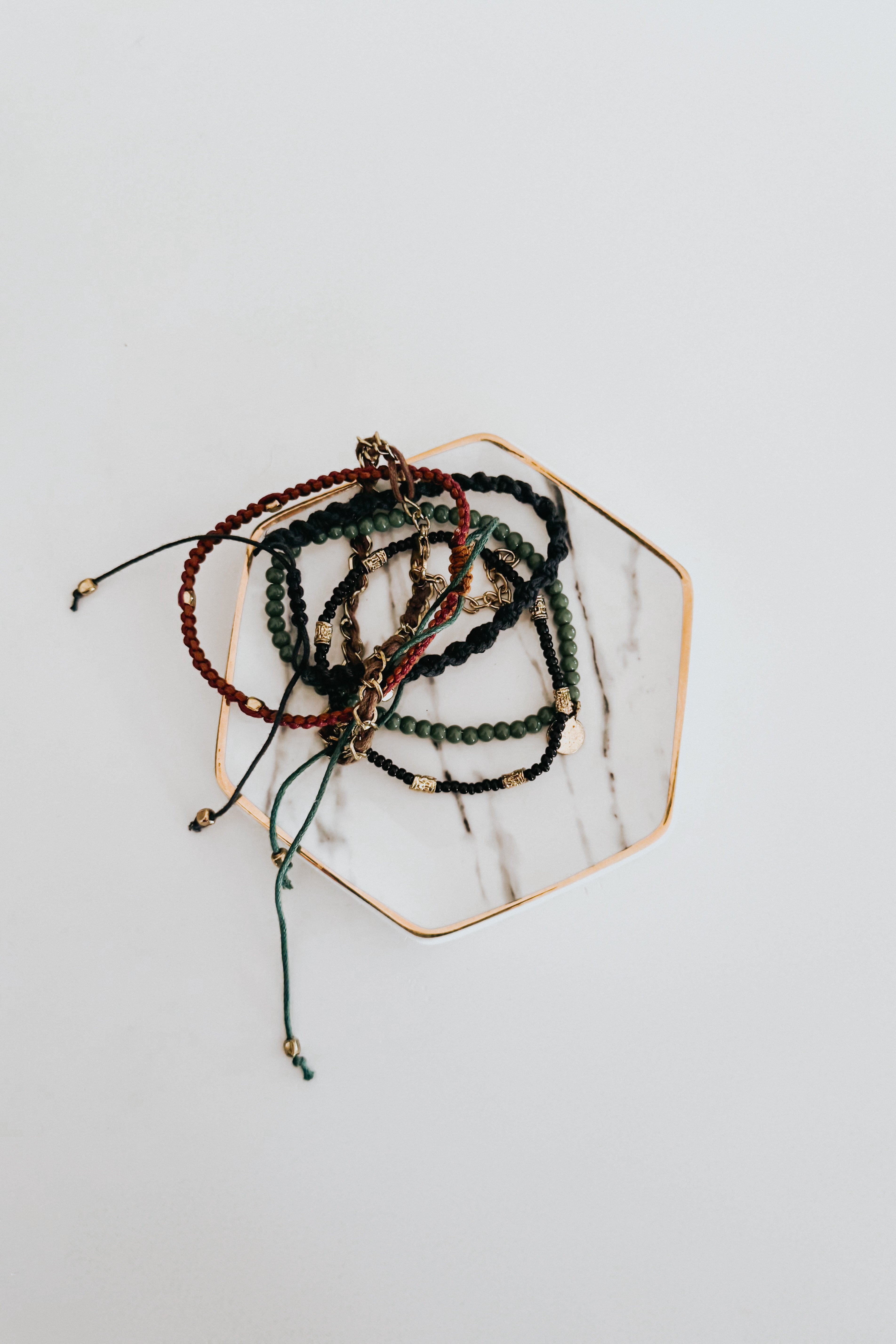 Collection of Ember Stackable bracelets with braided cords and varied beads arranged on marble hexagonal tray
