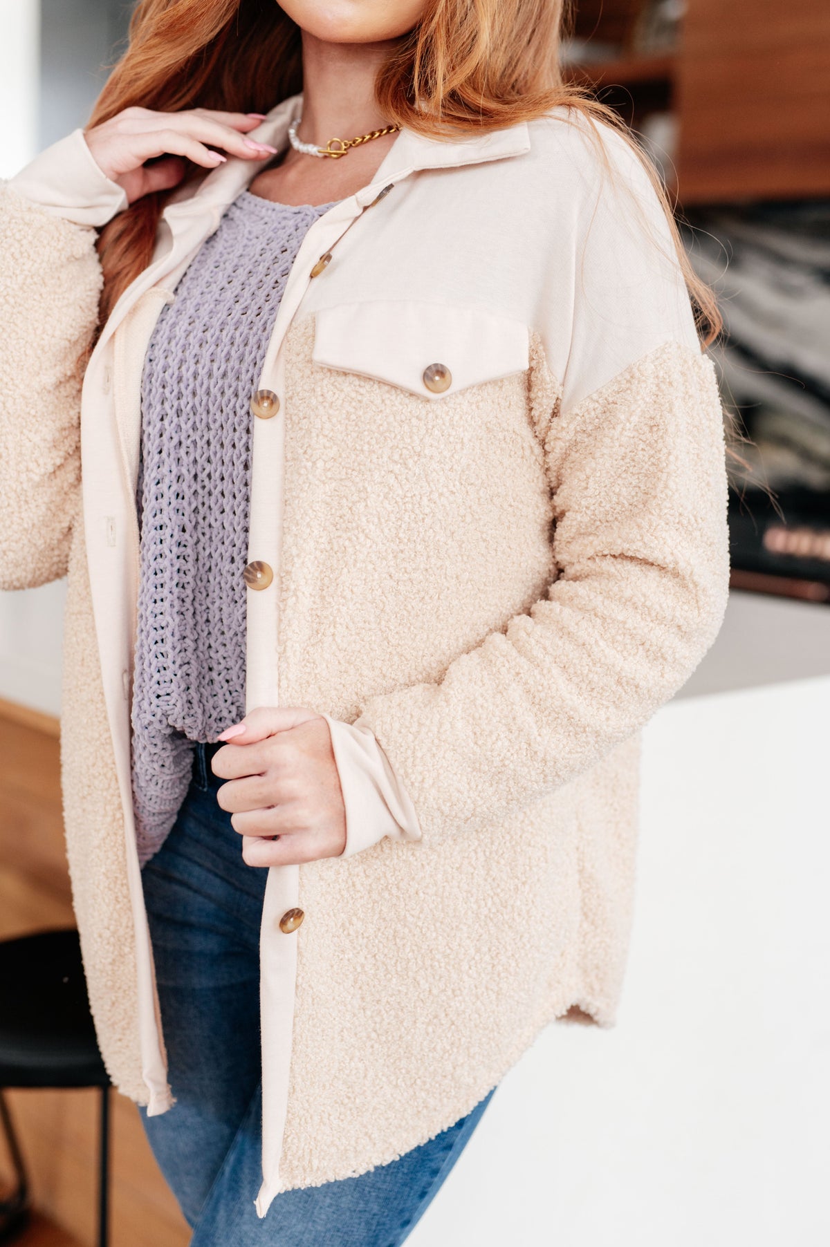 Woman wearing a cream sherpa shacket with faux chest pockets over a lavender knit sweater and blue jeans indoors
