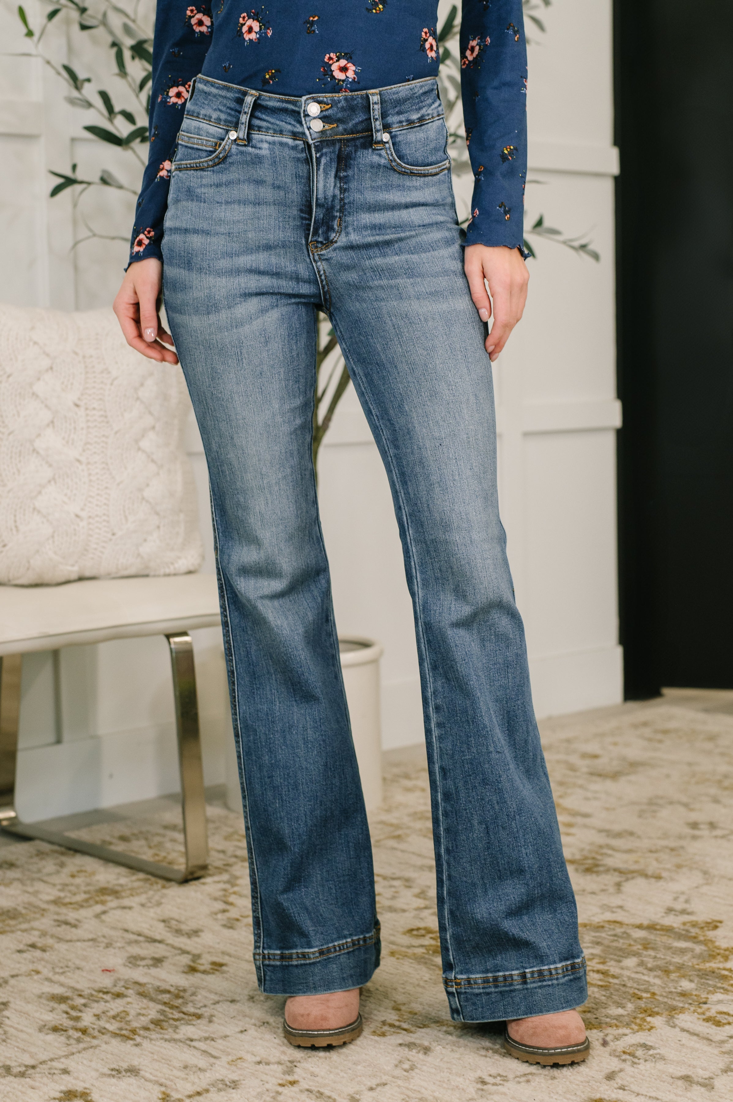 Front view of woman wearing blue high-rise flare jeans with double button closure and cuffed hems indoors