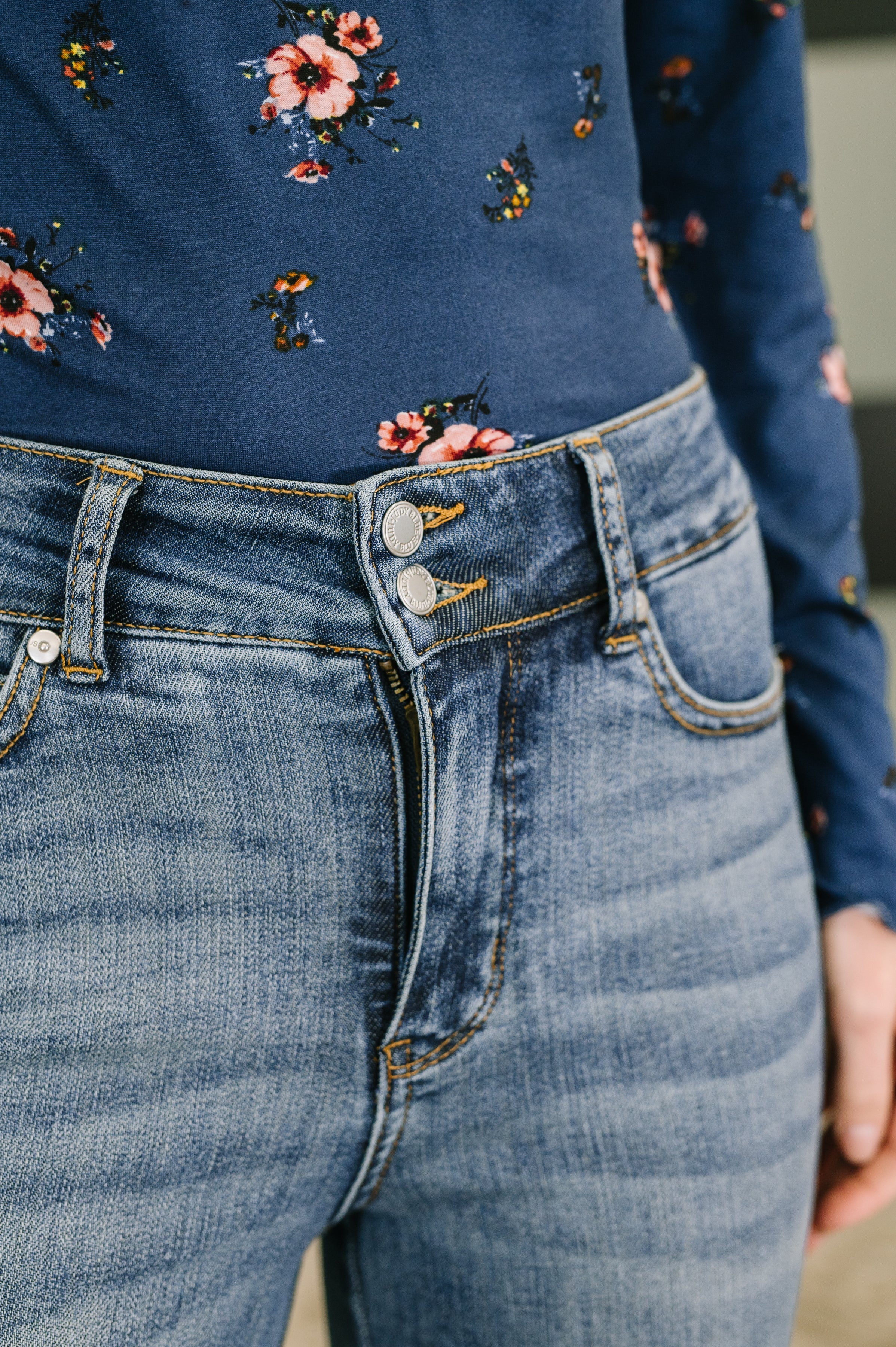 Close-up of high-waist blue denim jeans with double button and faded detailing worn with floral top