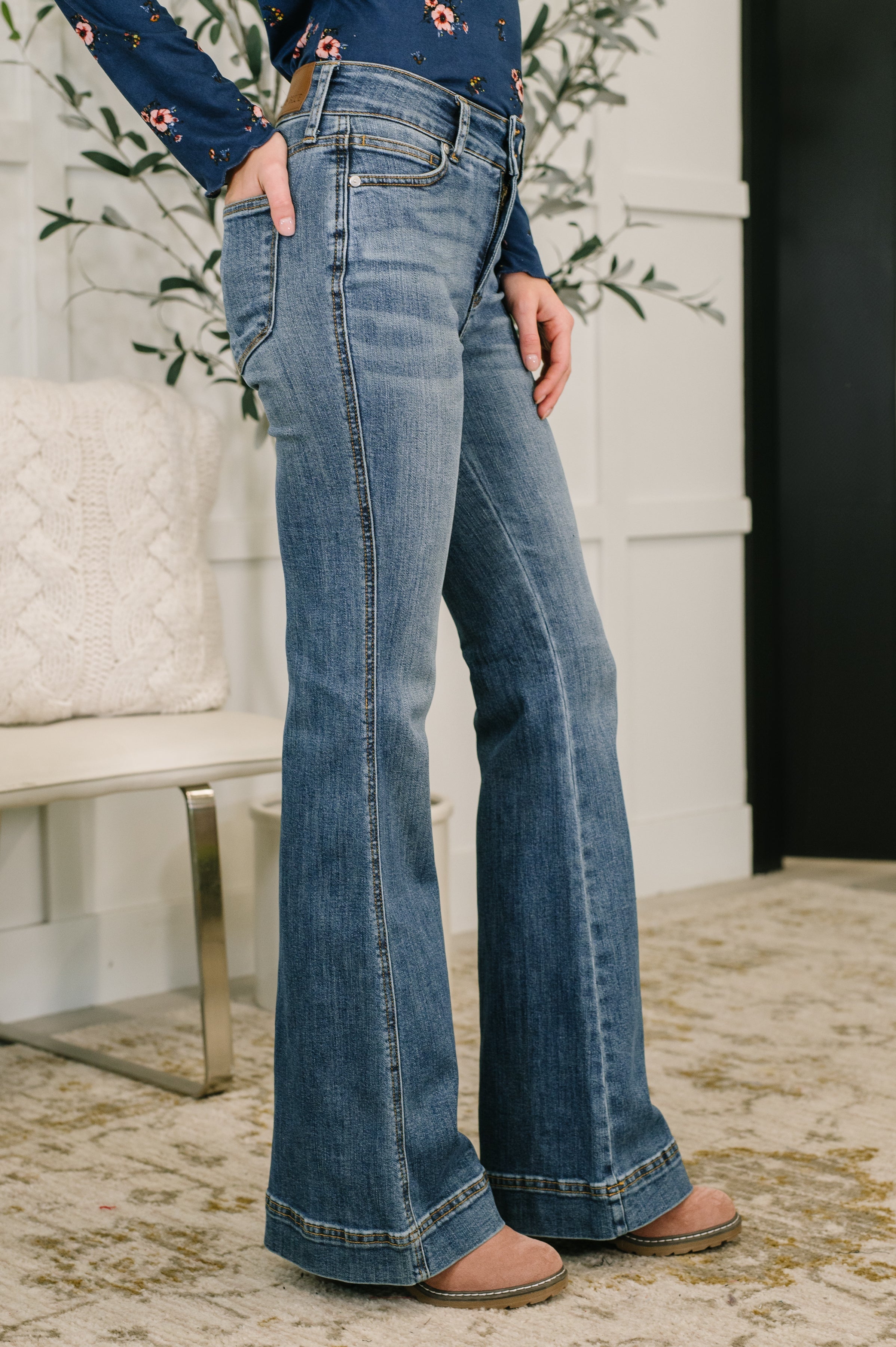 Side view of woman wearing faded blue high-rise flare jeans paired with brown shoes indoors