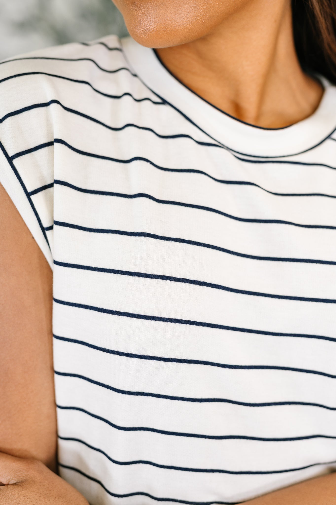 Close-up of ivory striped cap sleeve tee in soft fabric on model with warm skin tone in eclectic style setting
