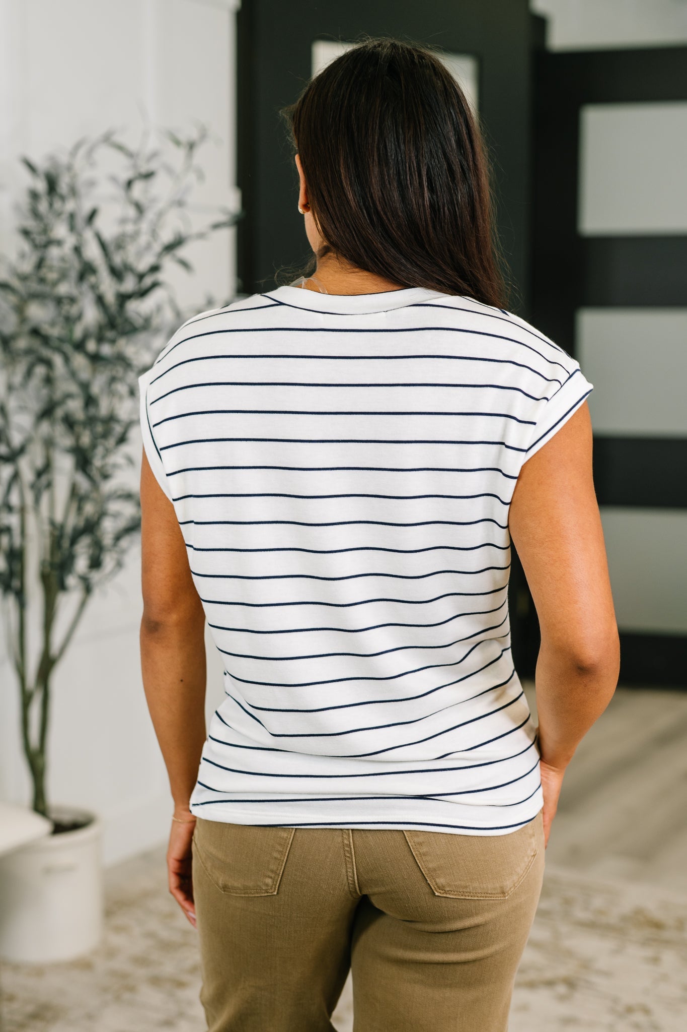 Back view of woman wearing ivory and navy striped cap sleeve tee styled with olive pants in eclectic setting