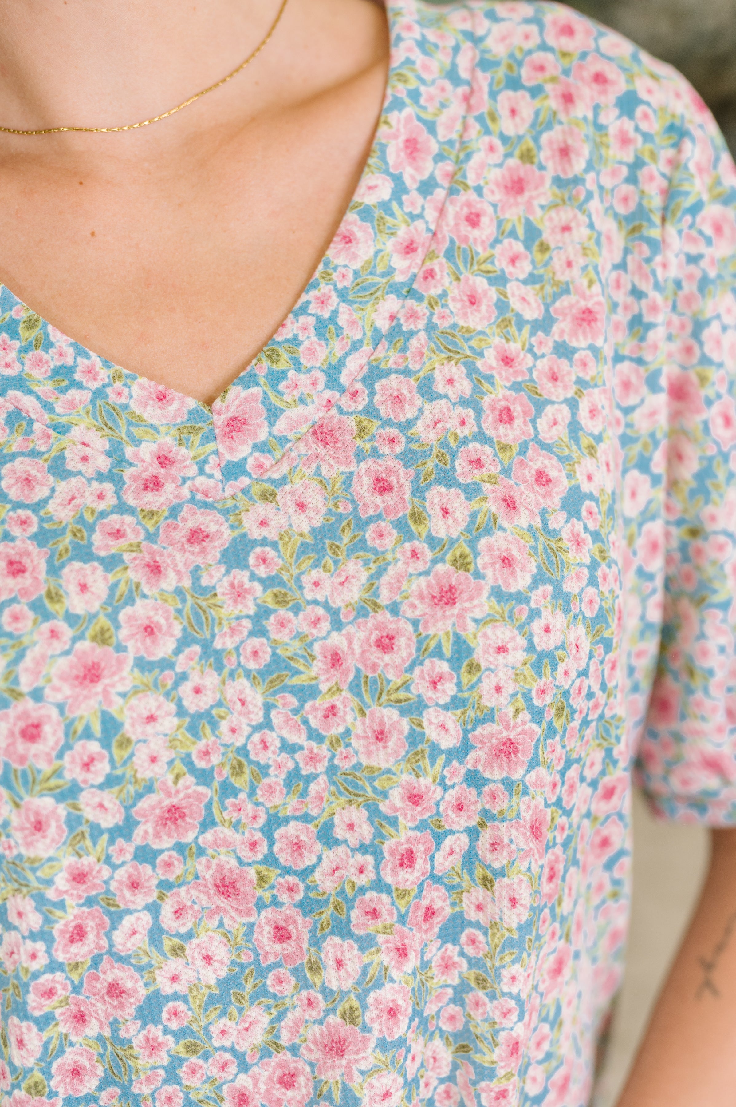 Close-up of blue waffle knit blouse with pink floral print and banded V-neckline on woman's upper torso