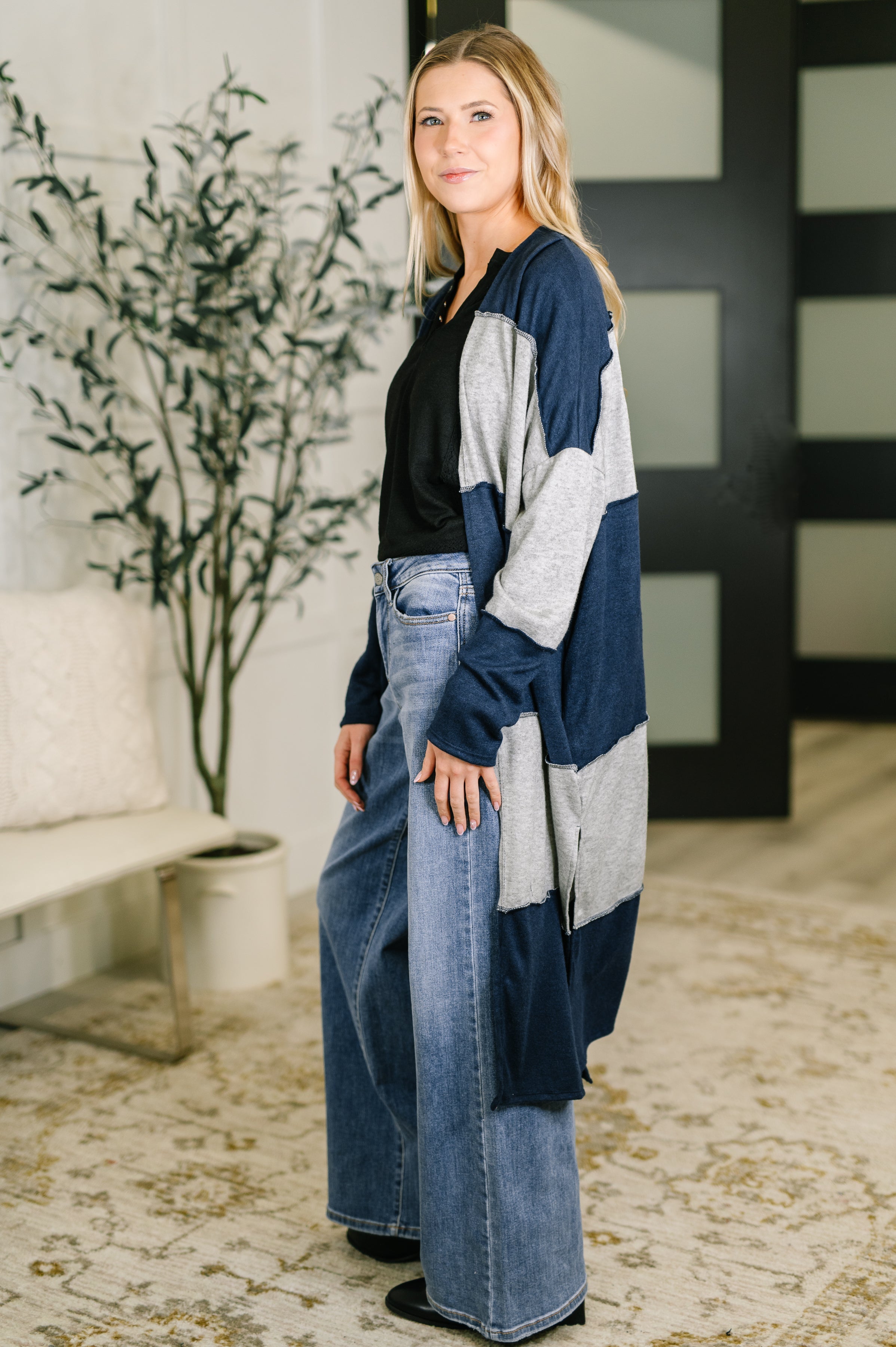 Woman wearing navy and gray color block long open front cardigan with wide-leg jeans indoors