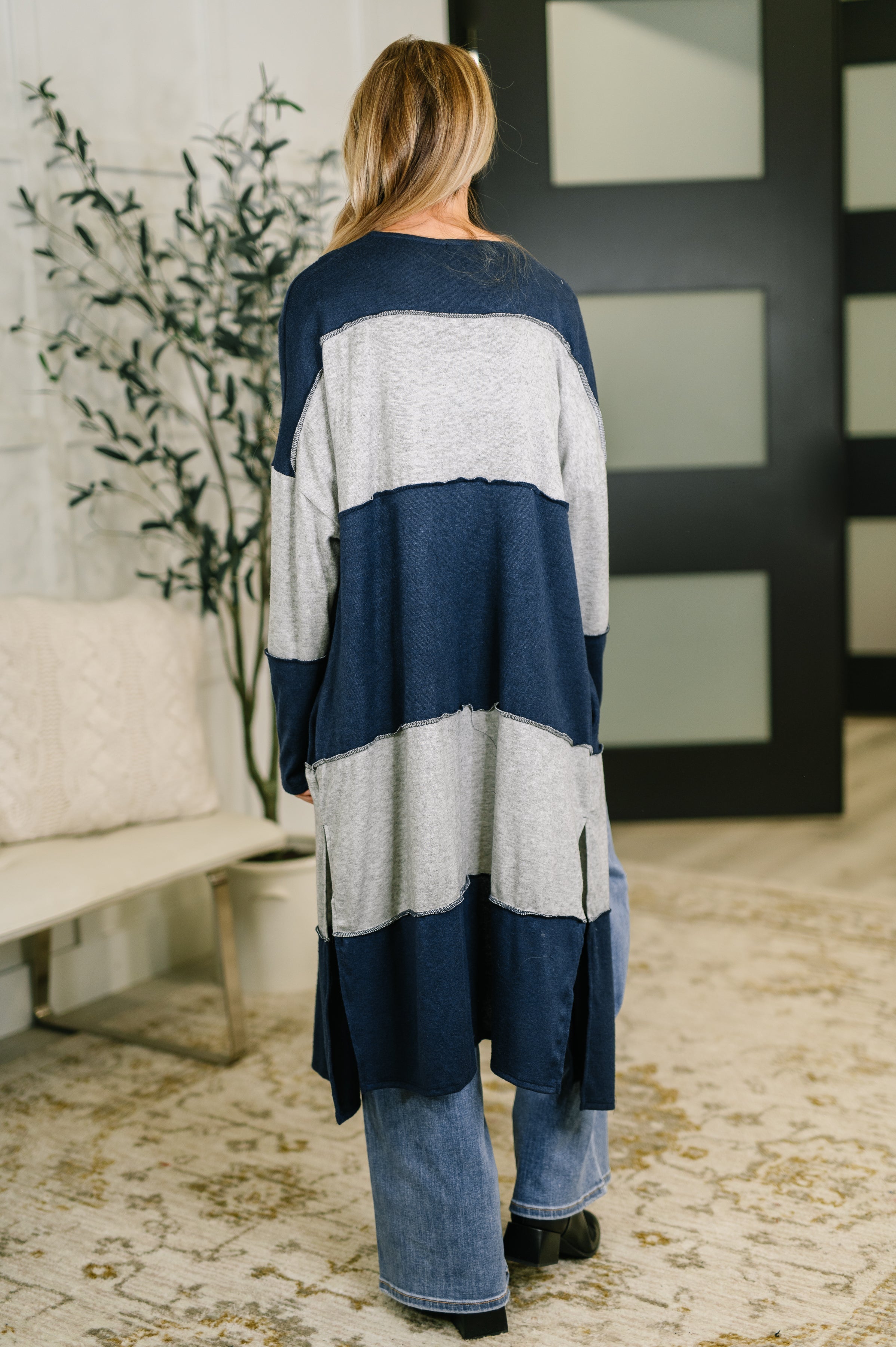 Woman wearing a long open front cardigan with navy and light gray color blocks standing indoors