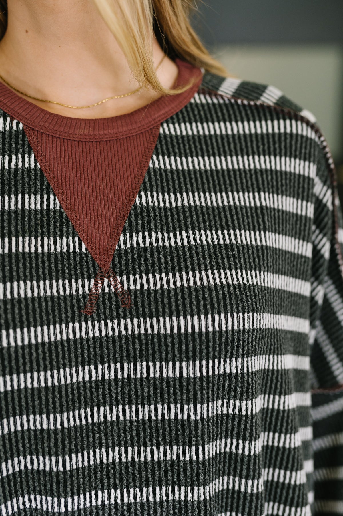 Close-up of a woman wearing a charcoal striped textured knit pullover with a rust contrast neckline and delicate gold necklace