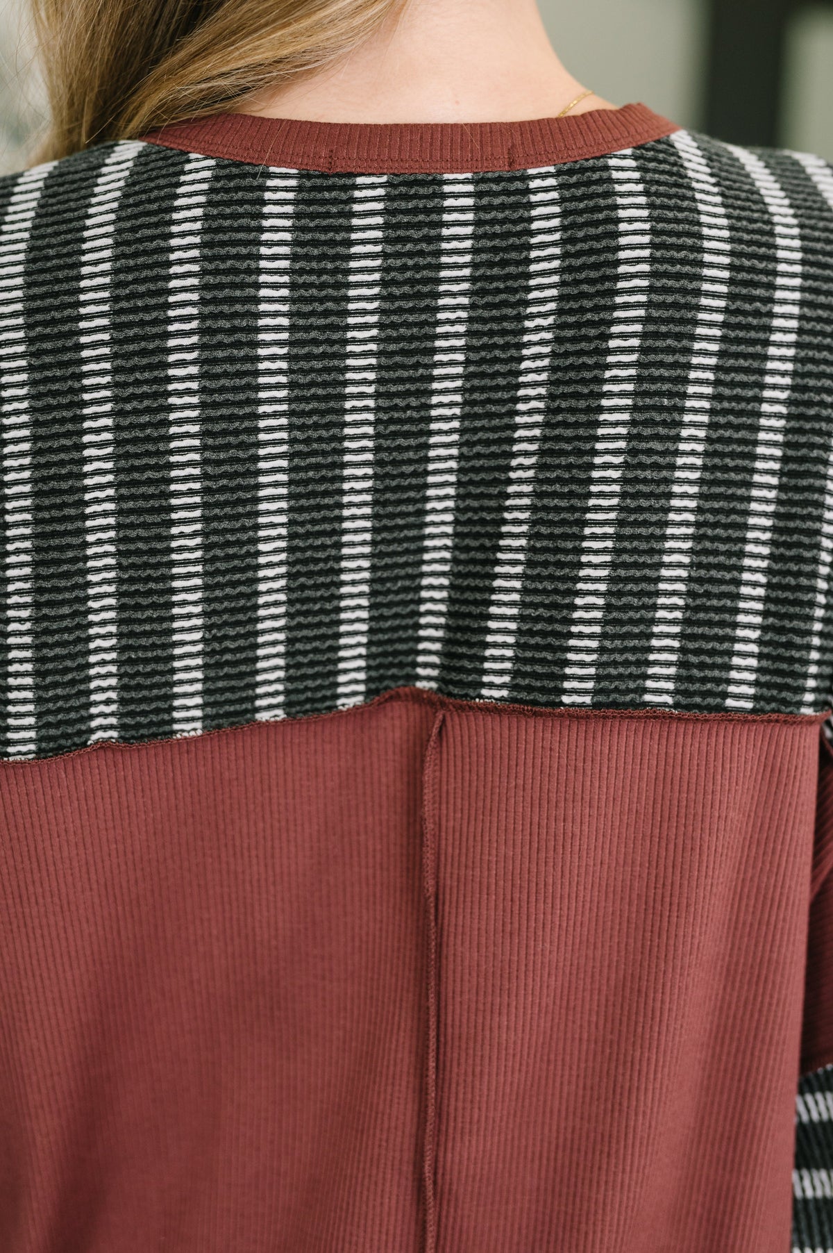 Back view of a woman wearing a charcoal and rust contrast textured knit pullover with a relaxed fit