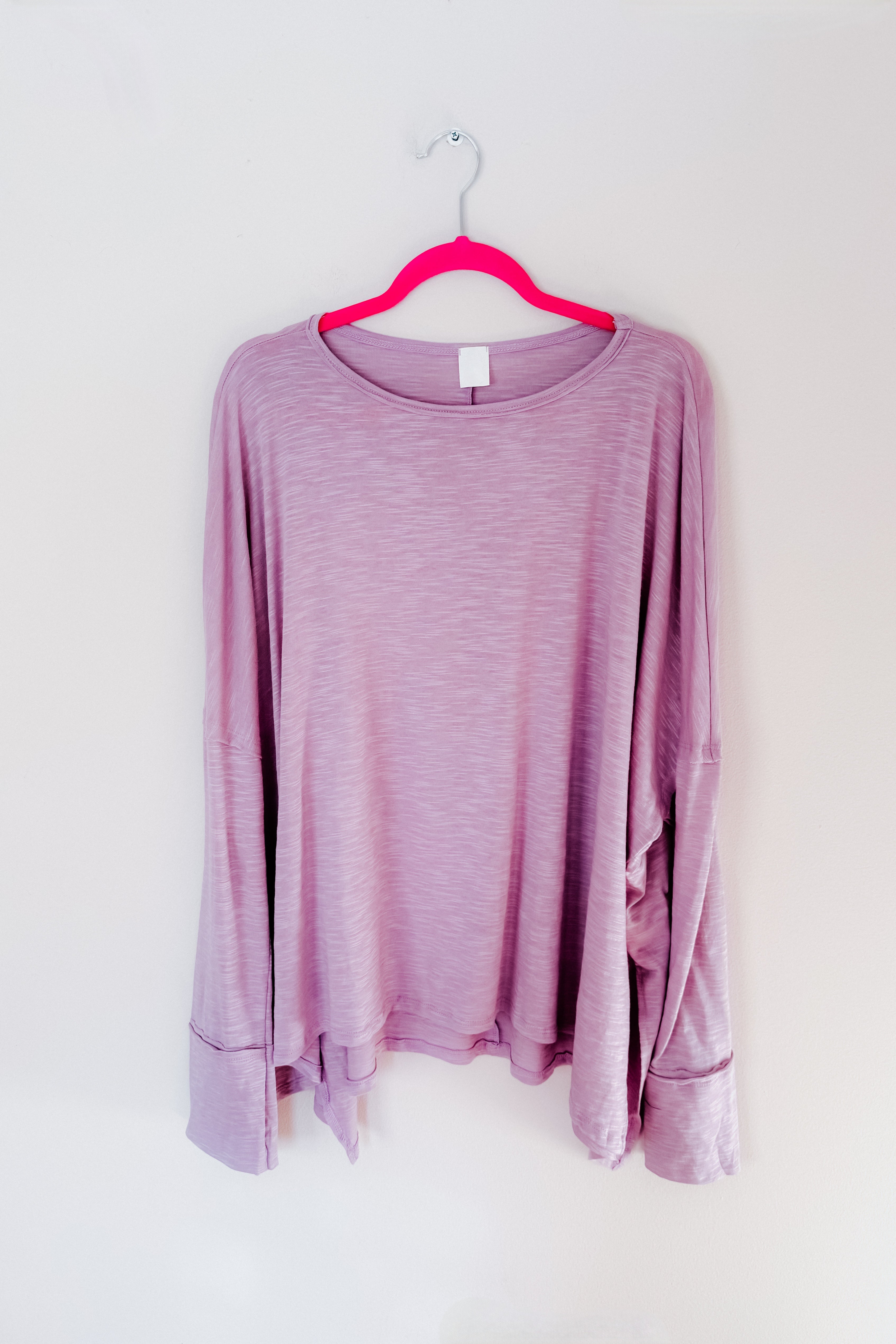 A lavender long sleeve top with a step hem hanging on a pink hanger on a white background