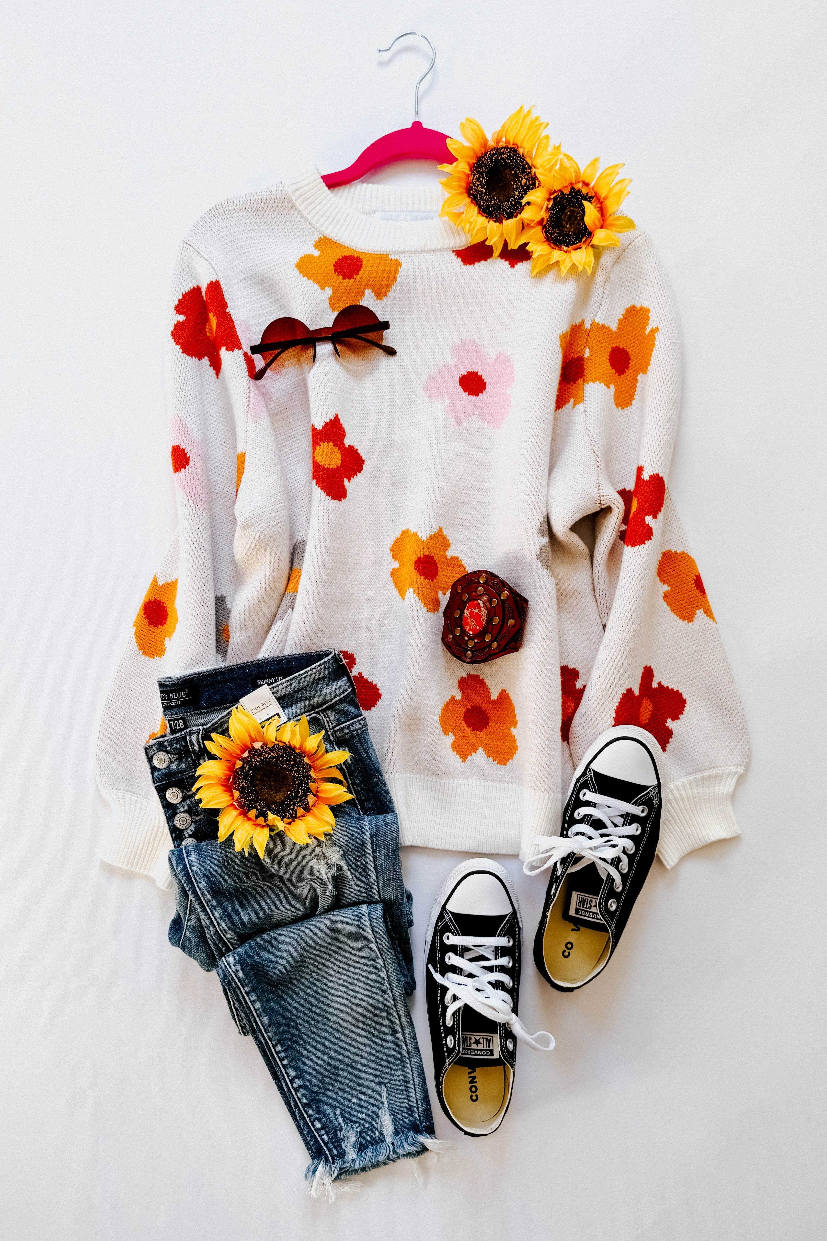 Cream floral sweater with orange and red flowers paired with distressed blue jeans and black sneakers flat lay
