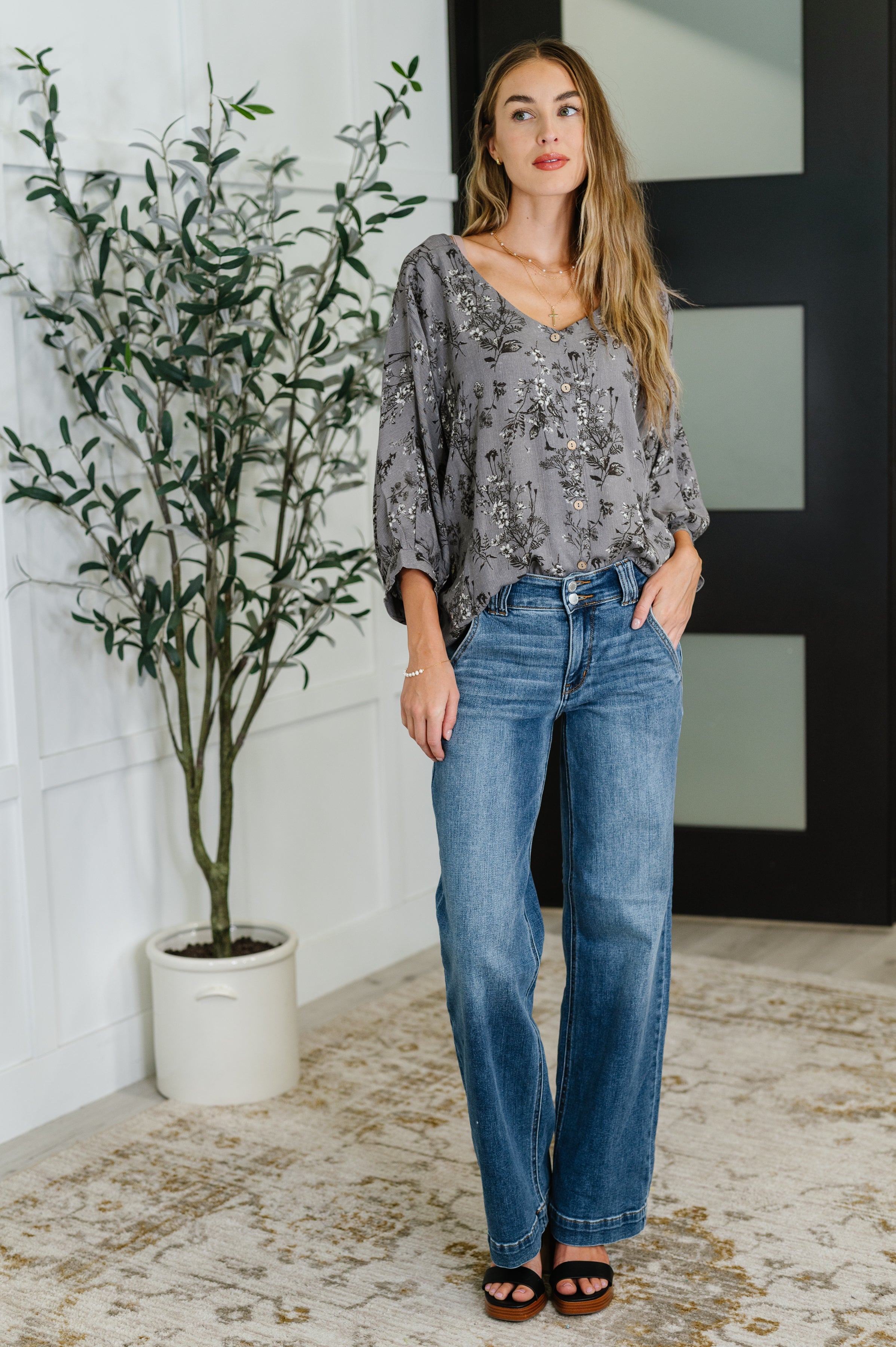 Woman wearing loose dune grey crinkle woven blouse with black floral print tucked into high-waisted blue jeans indoors