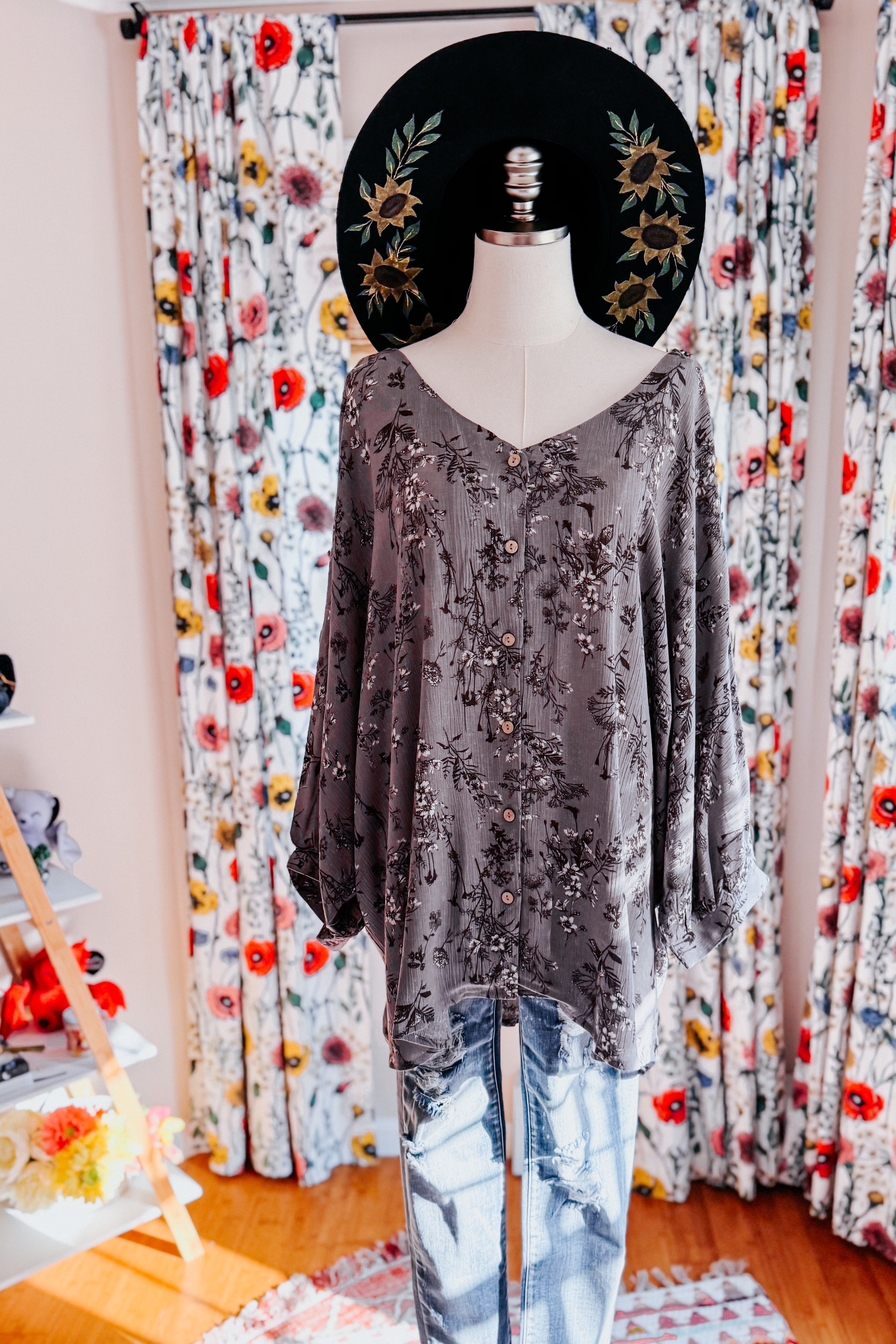Dune grey crinkle woven blouse with muted floral print displayed on mannequin with black floral hat indoors