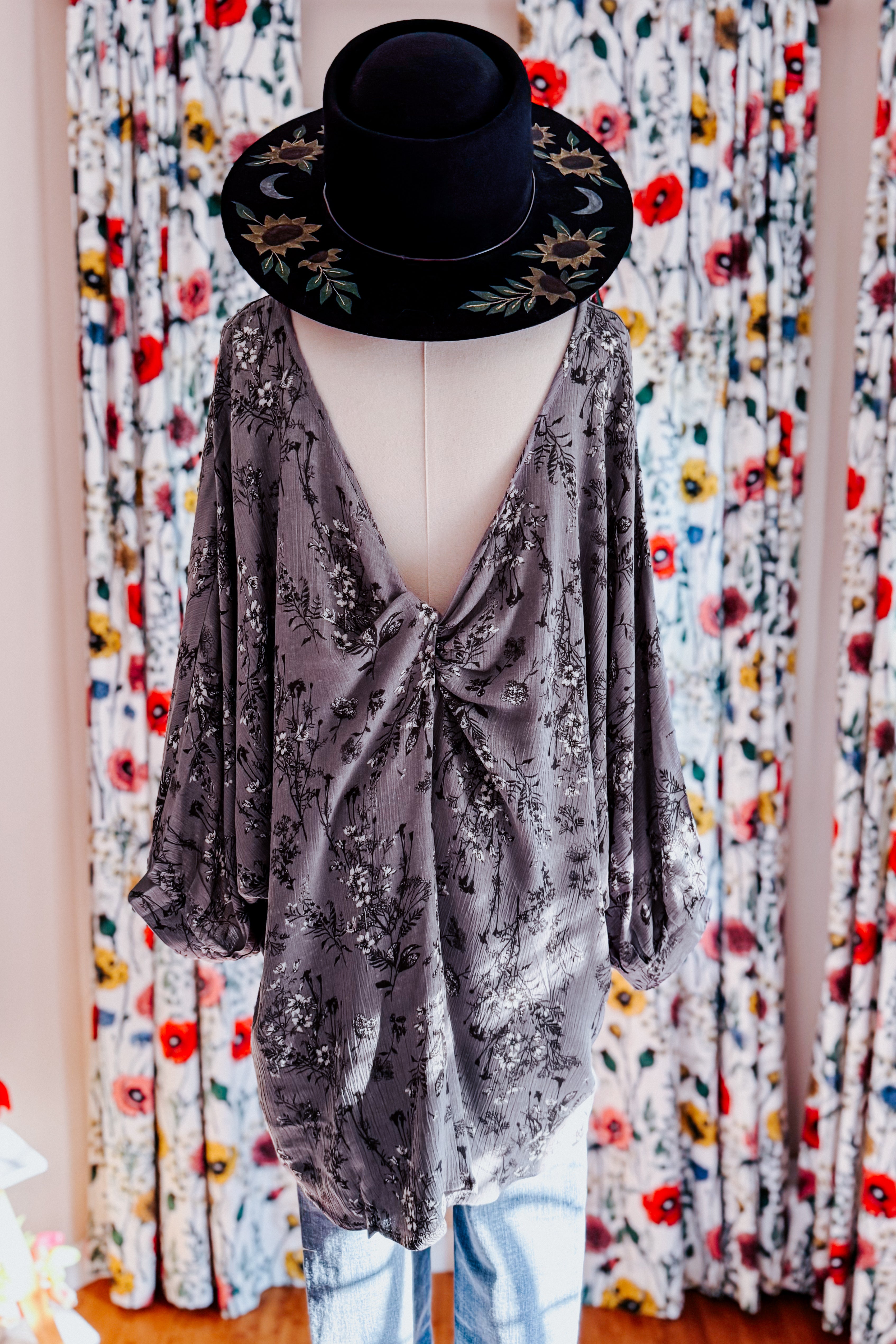 Dune grey crinkle blouse with dark floral print and deep back V-neck displayed on dress form with black embroidered hat