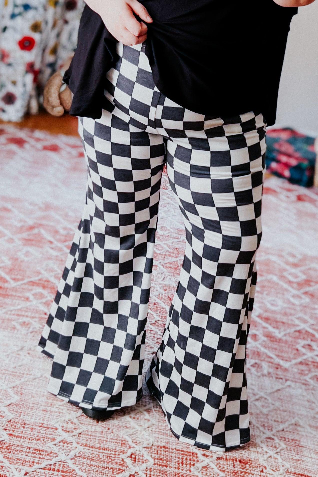 Woman wearing black and white checkered flared pants standing on patterned rug indoors