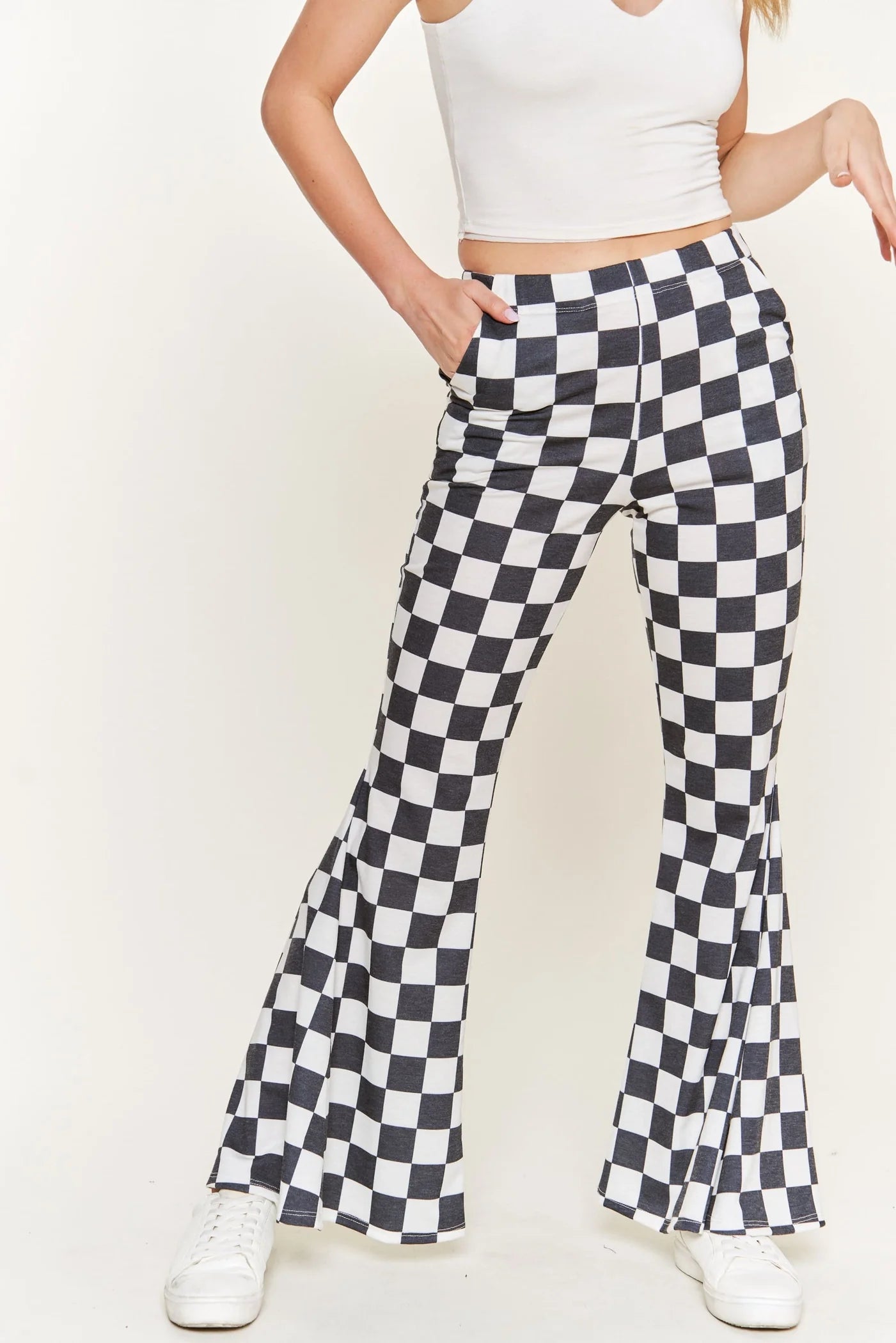 Model wearing black and white checkered flared pants with side pockets and white sneakers against plain background
