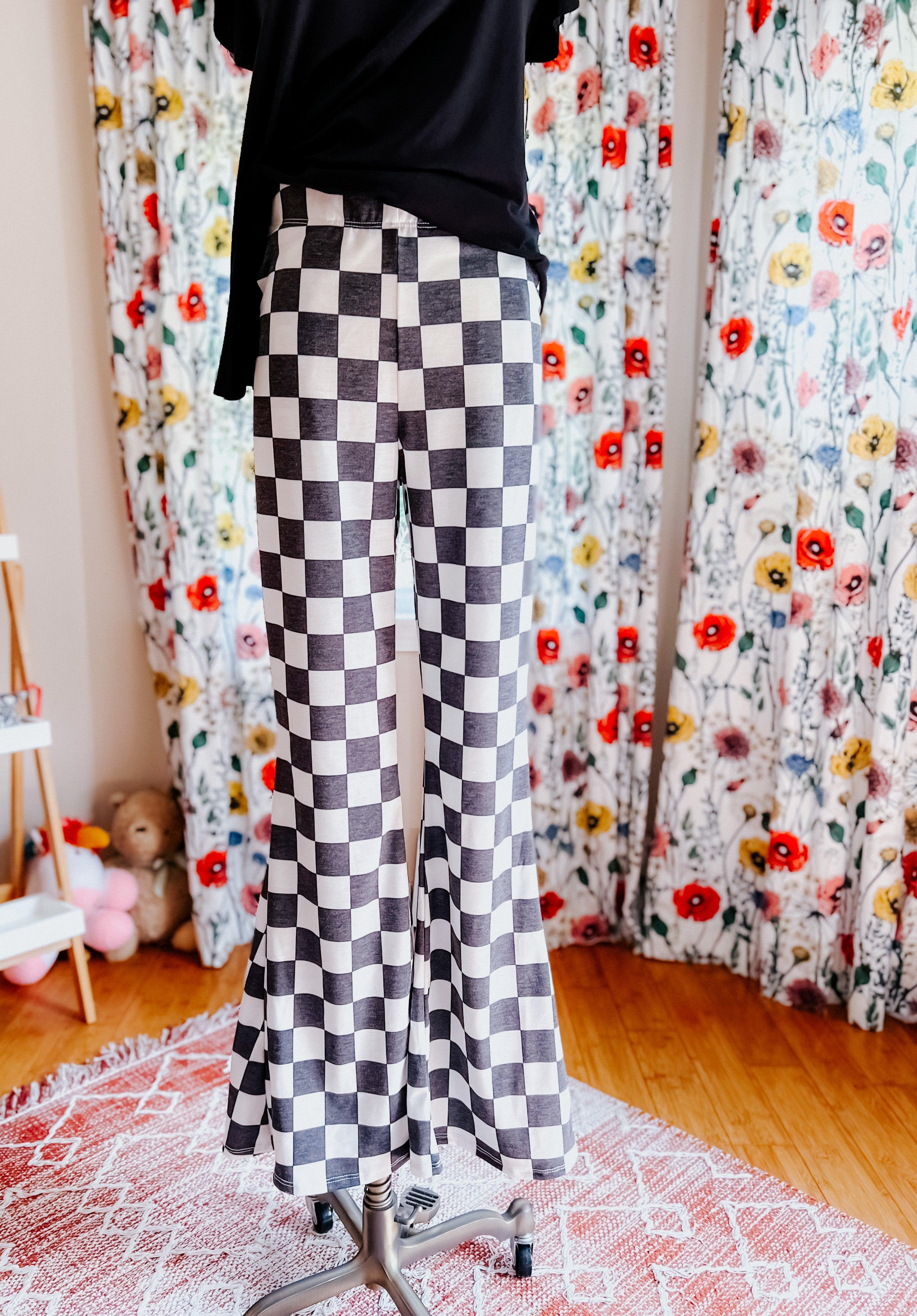 Black and white checkered flared pants displayed on mannequin in room with floral curtains and patterned rug