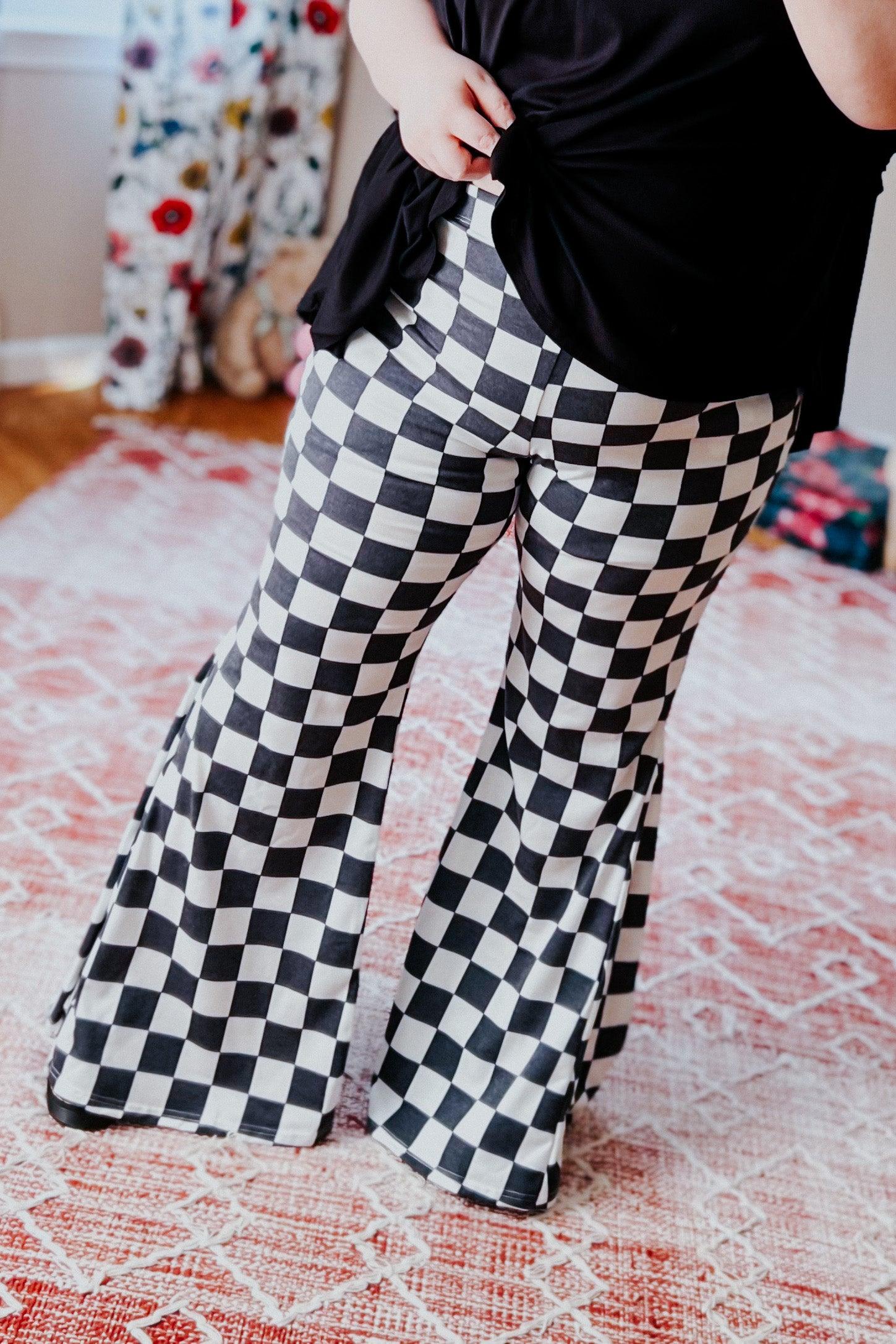 Woman wearing black and white checkered flared pants standing on patterned rug indoors with black top