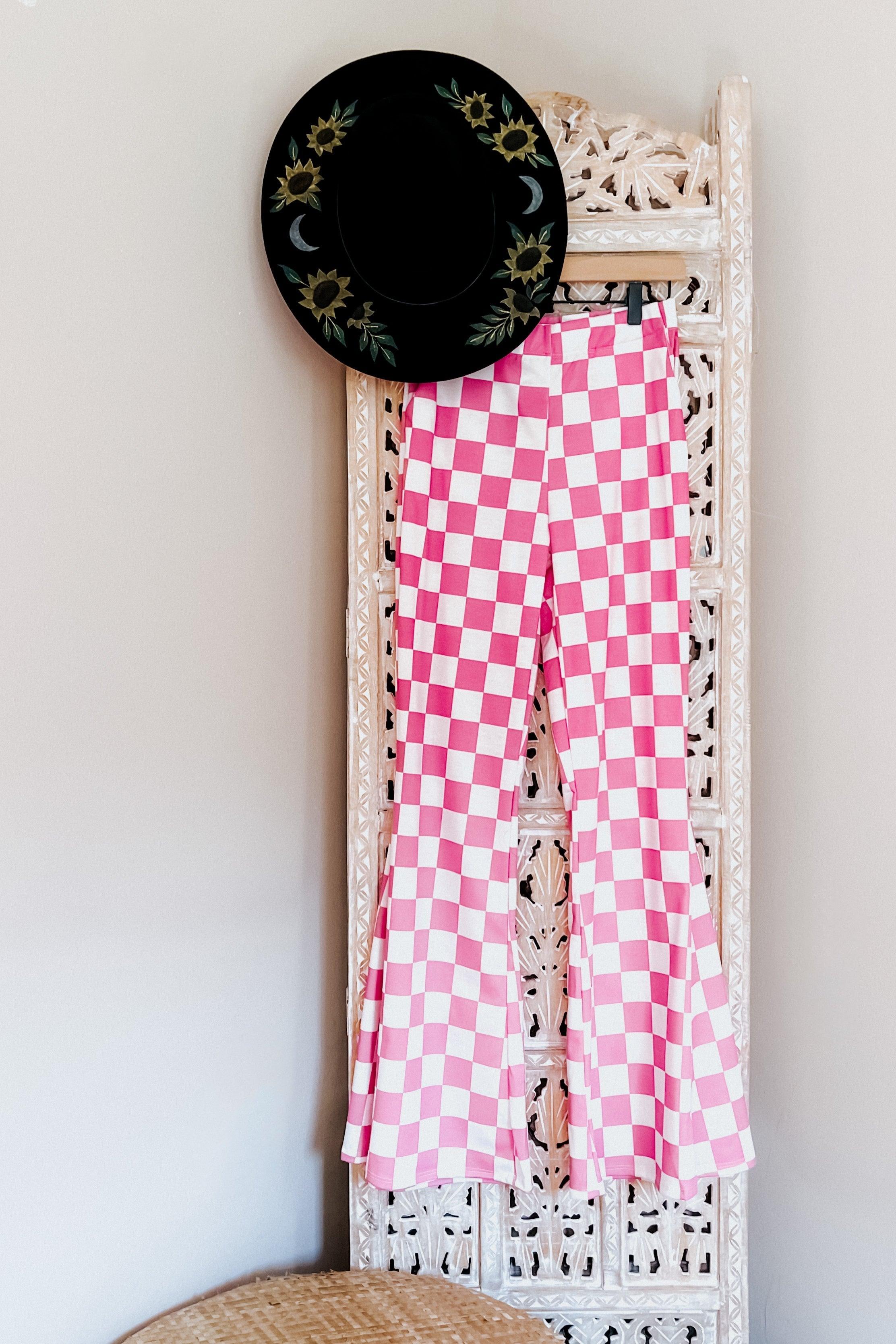 Pink and white checkered flared pants hanging on carved white room divider with black floral wide-brim hat