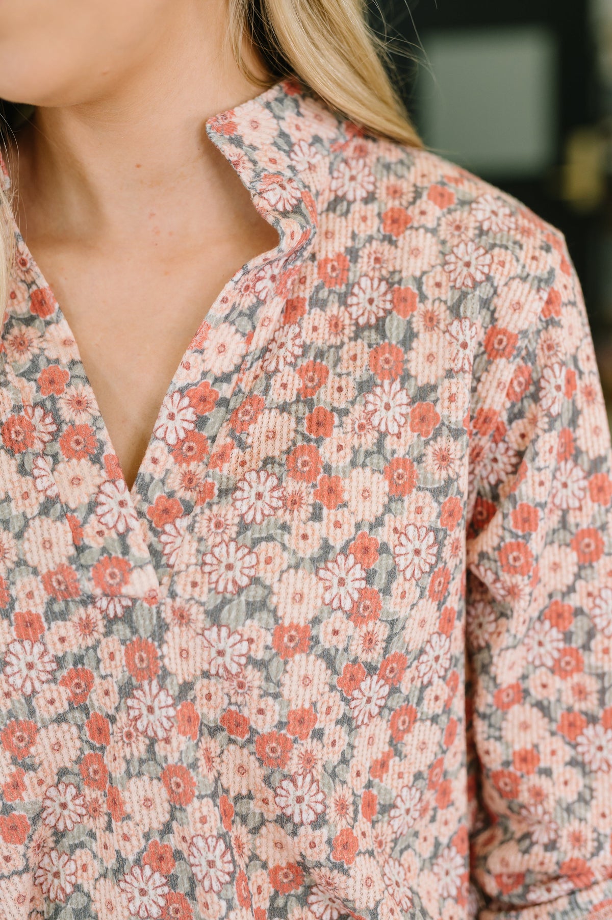 Close-up of a woman wearing a peach floral top with a split neckline and soft textured knit fabric