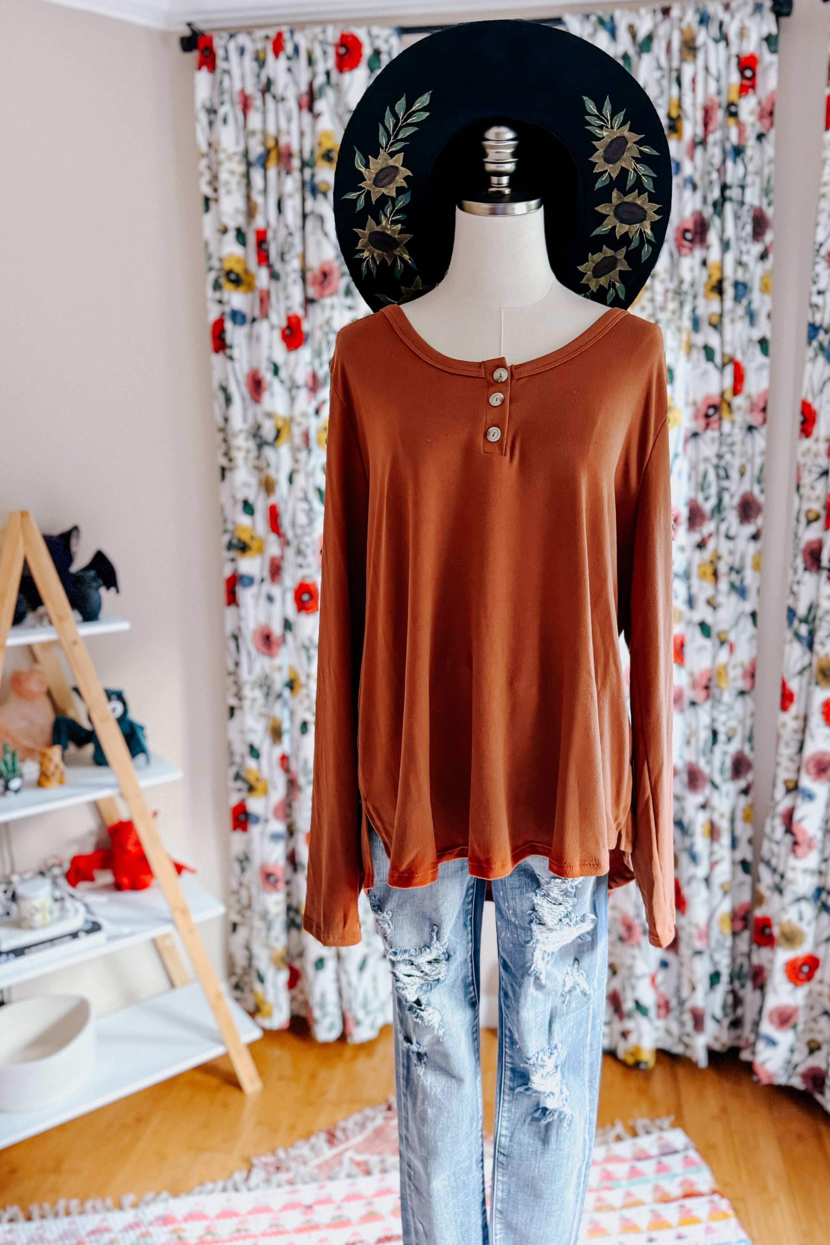 Mannequin wearing a rust scoop neck top with button placket paired with distressed light wash jeans indoors