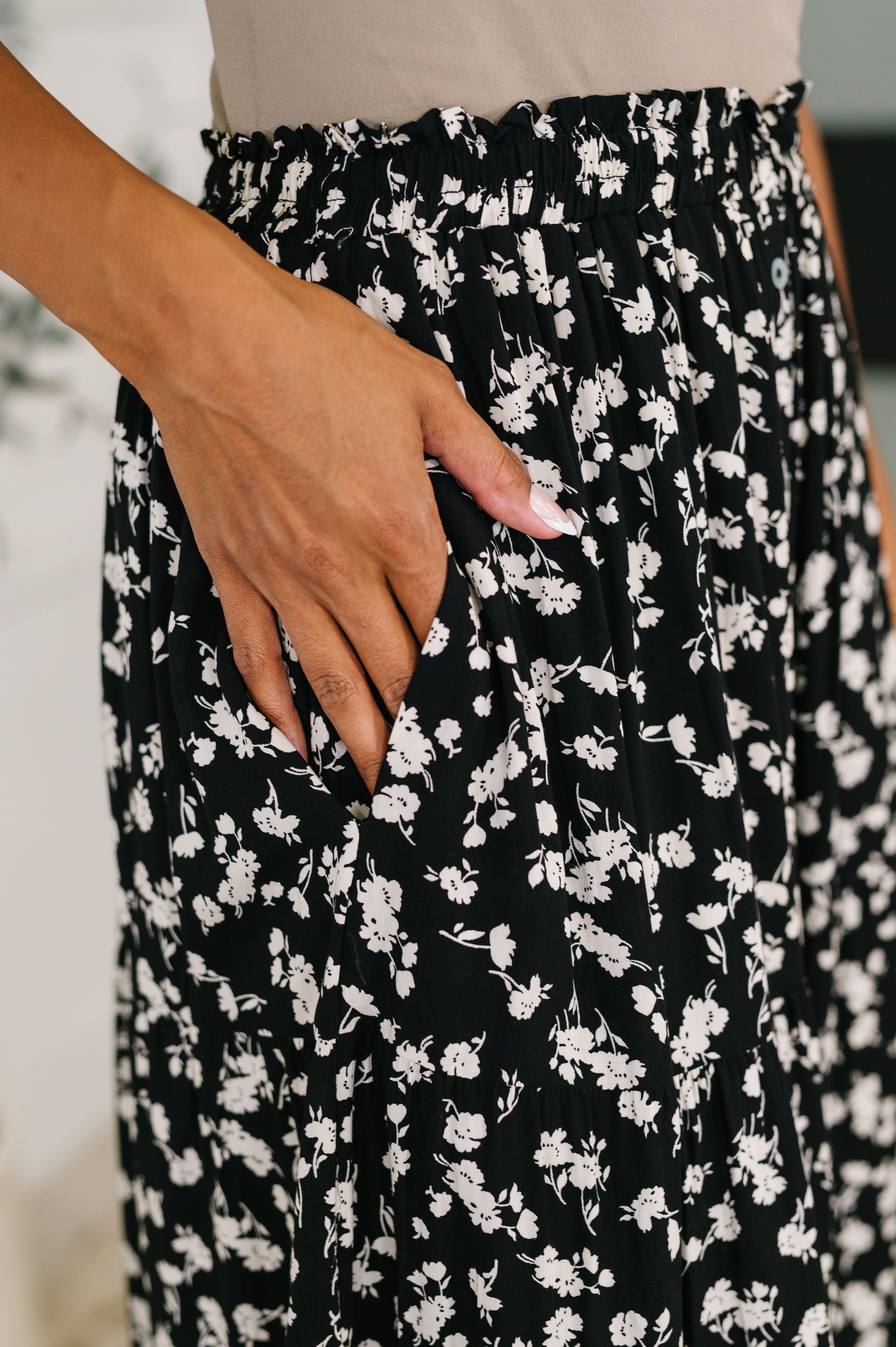 Close-up of hand resting in side pocket of a black floral skirt with lightweight woven fabric and ditsy print