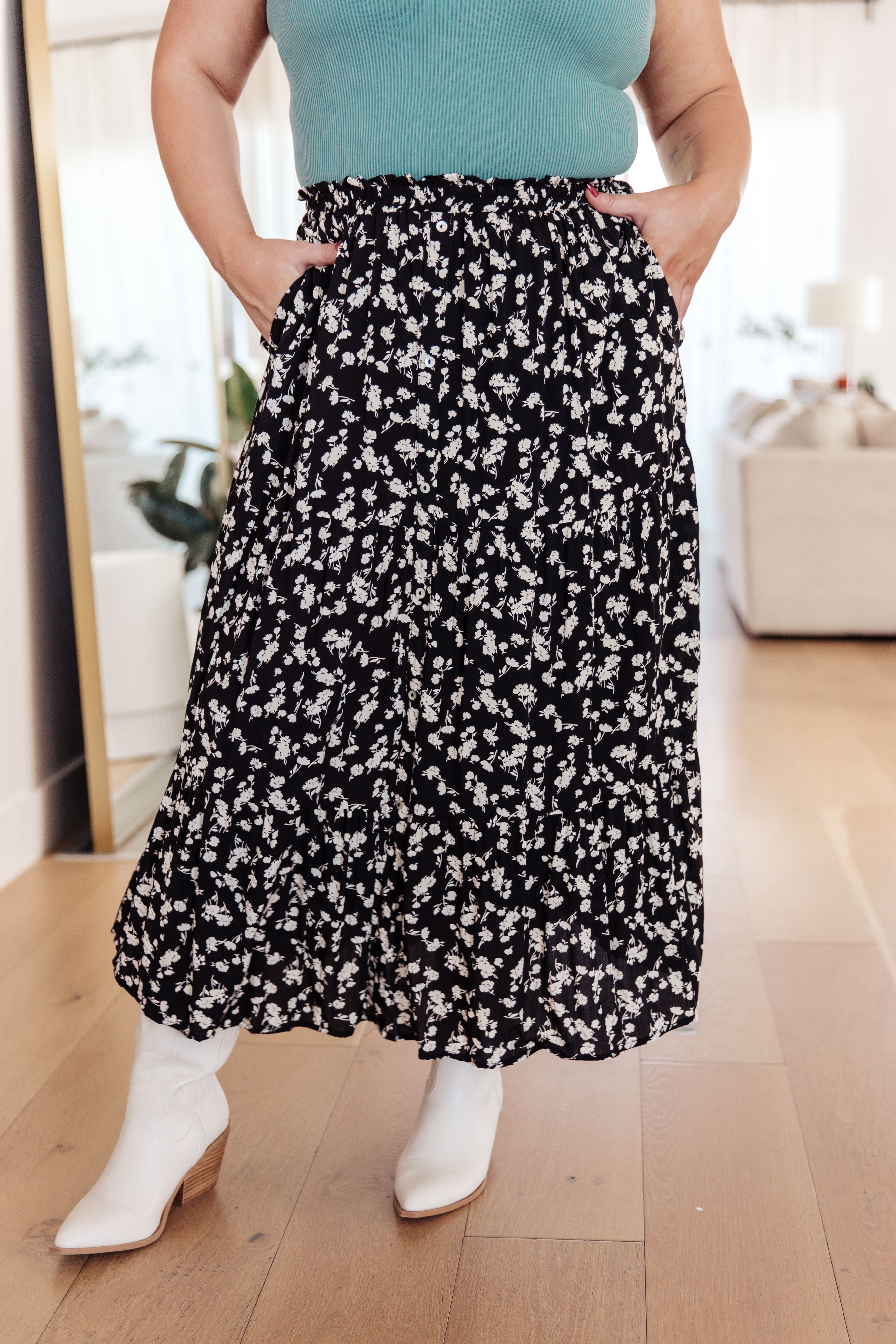 Woman wearing a black floral skirt with side pockets and white ankle boots in a bright indoor setting