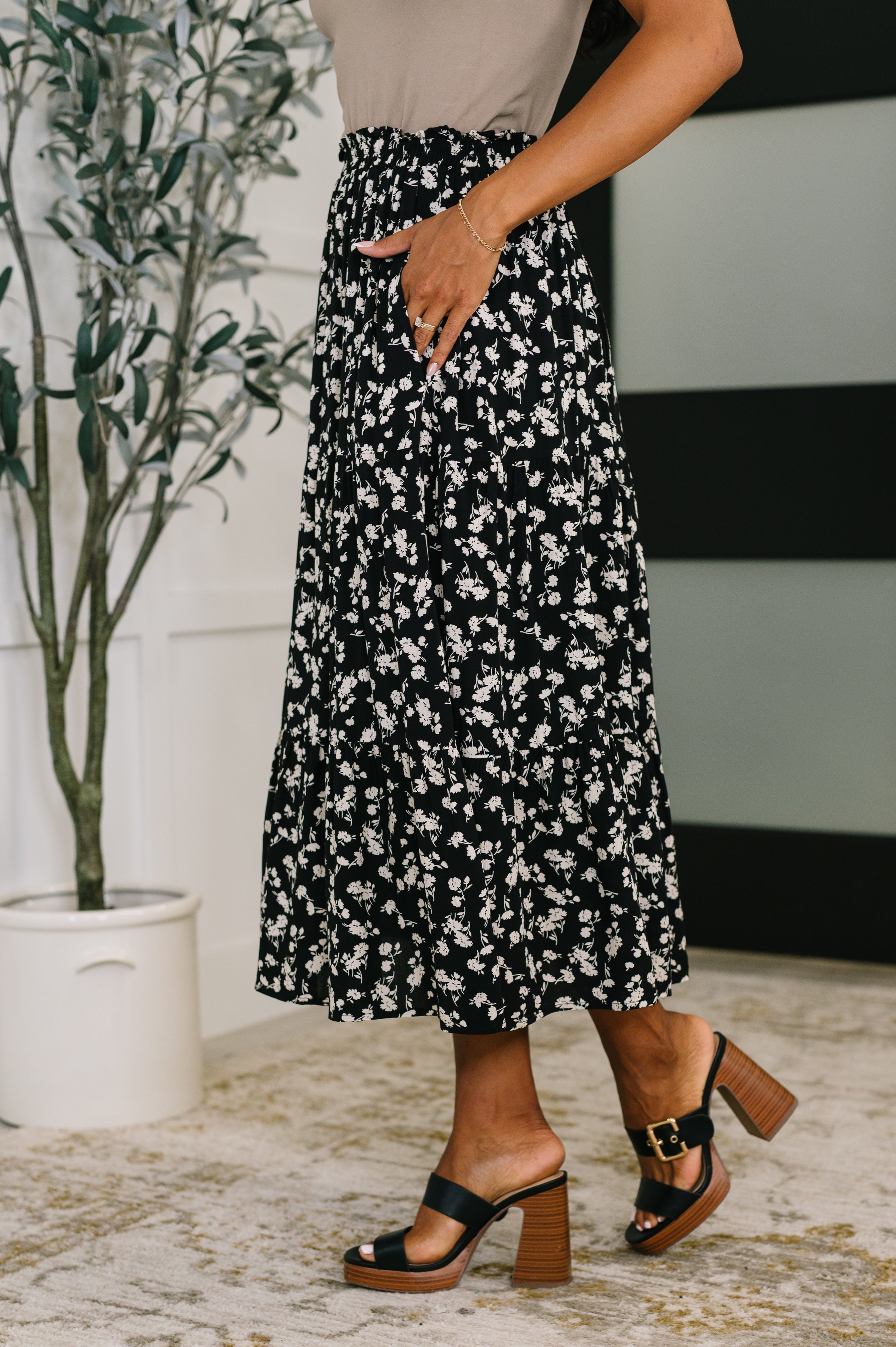 Woman wearing a black floral midi skirt with side pockets paired with black heeled sandals indoors