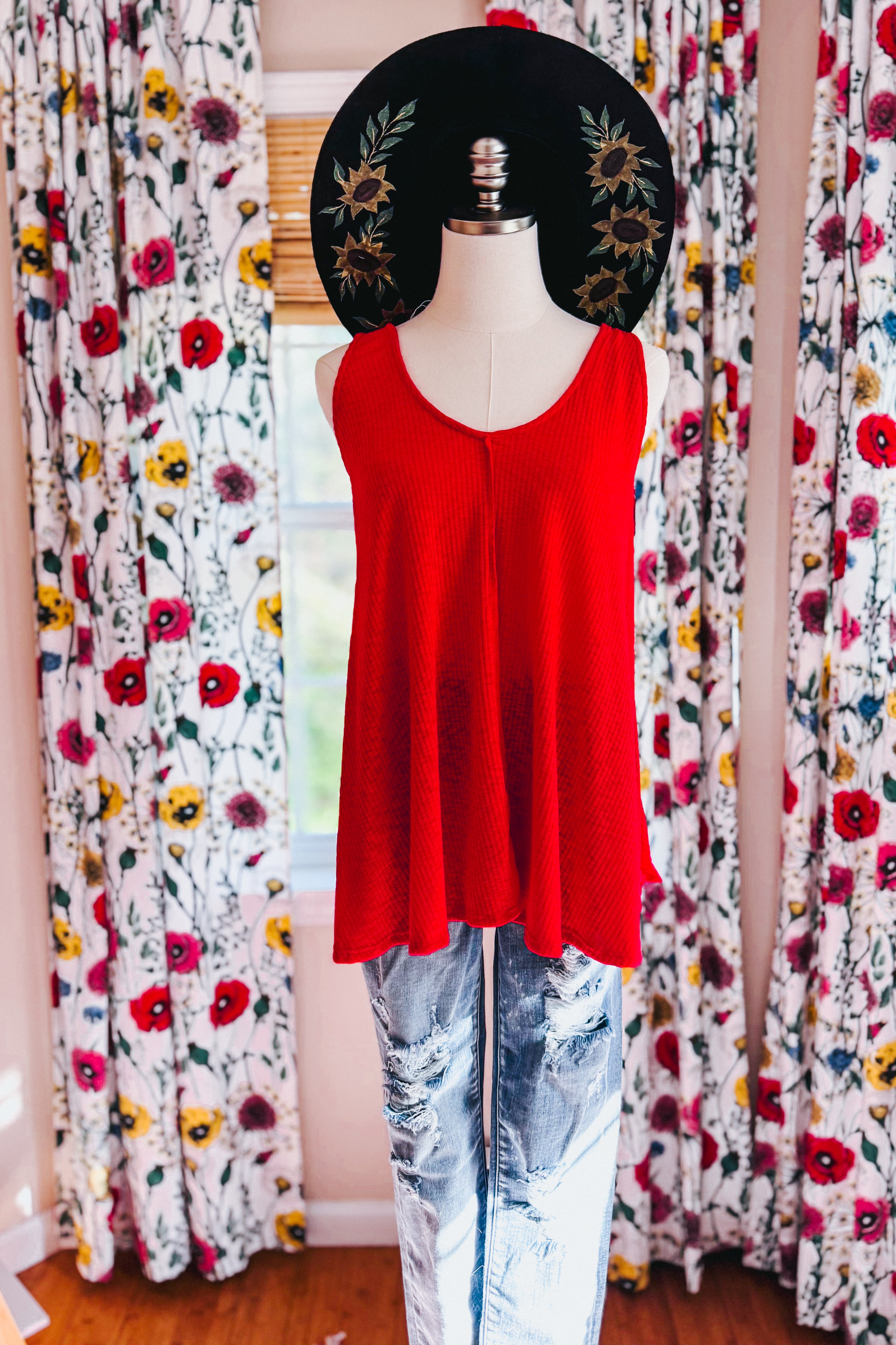 Red sleeveless ribbed tank top displayed on mannequin with distressed jeans and floral curtains background