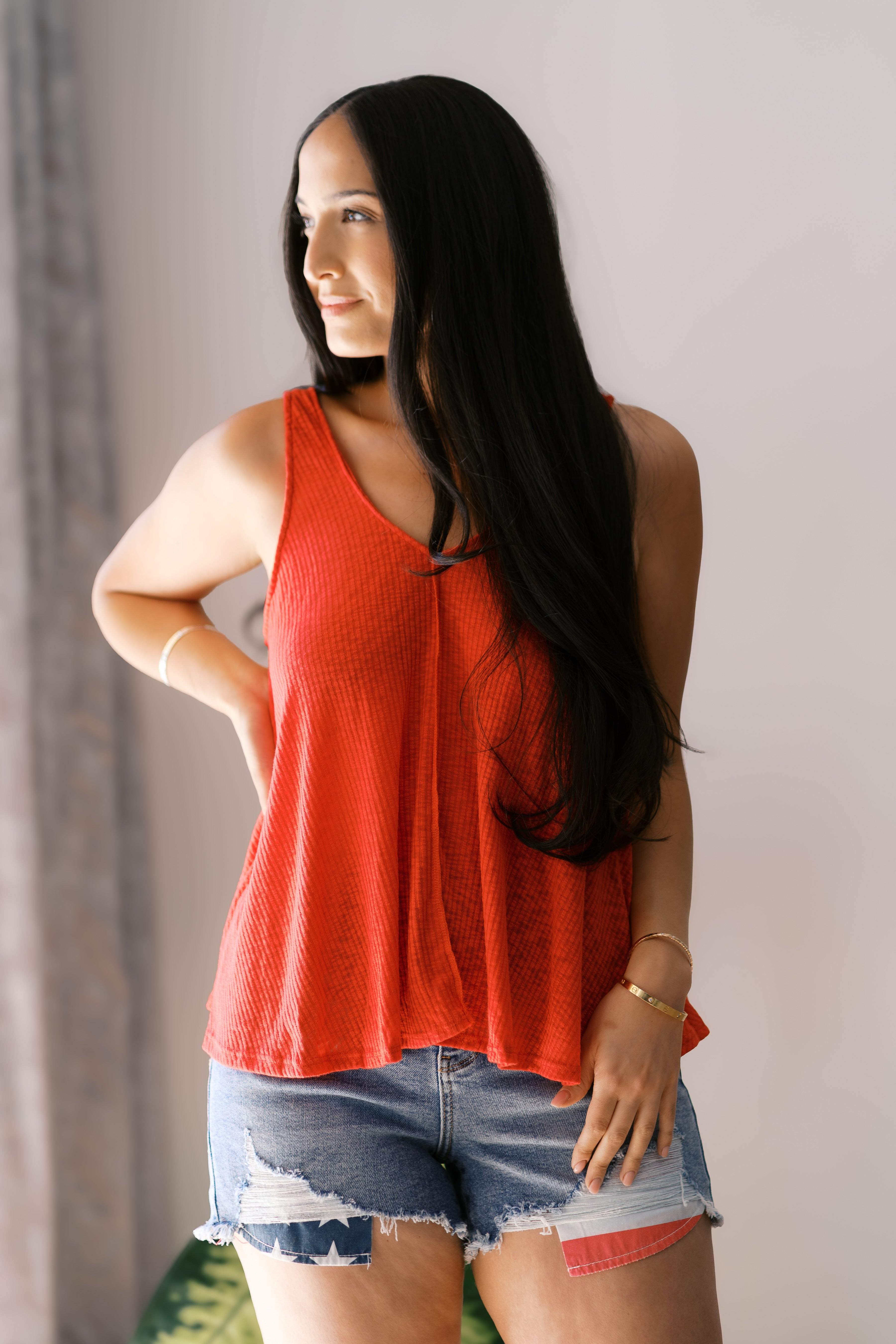 Woman wearing a flowy textured bright red sleeveless tank top with patchwork denim shorts indoors