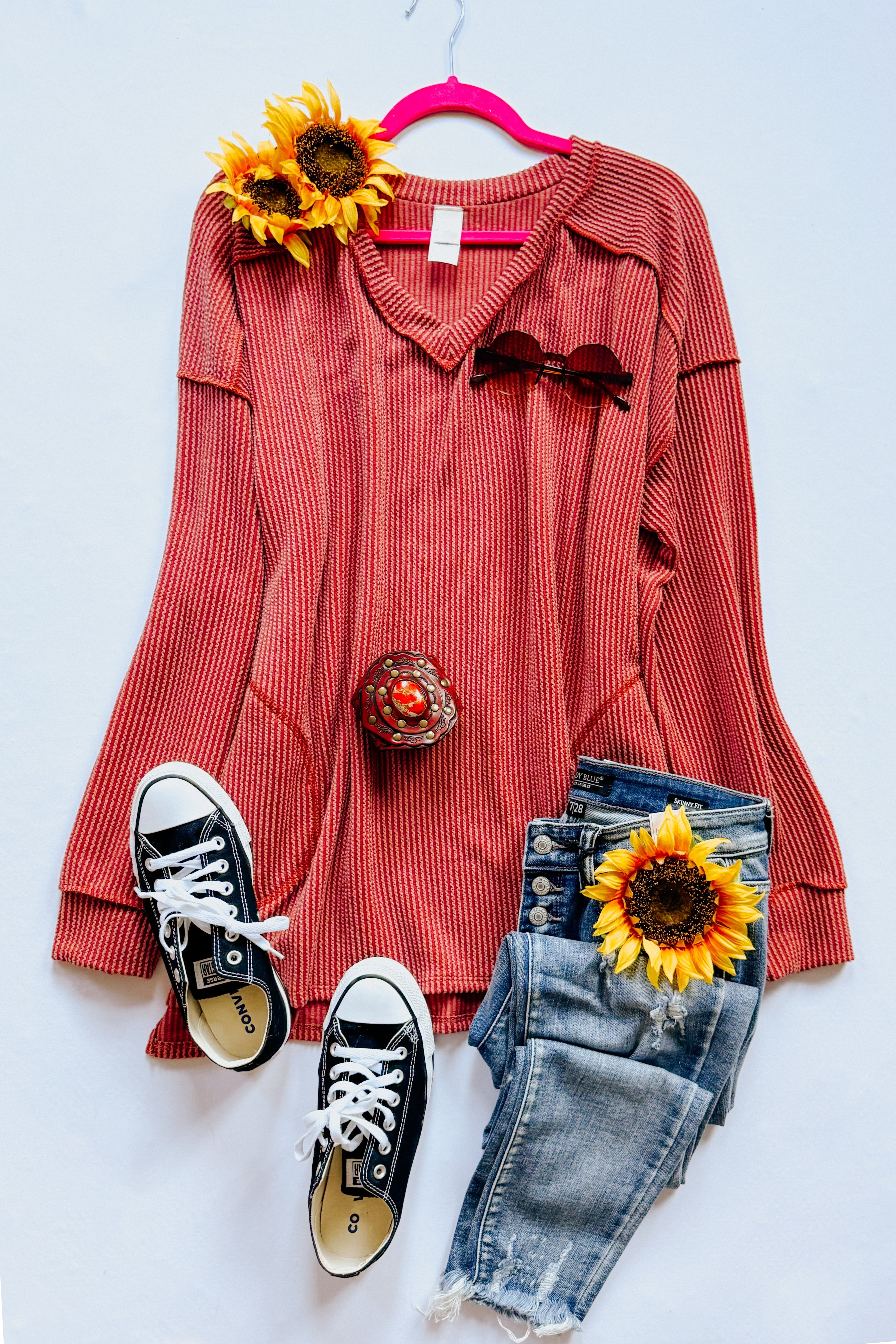 Rust ribbed First and Foremost Rib Knit Top with V-neck displayed flat with black sneakers, distressed denim shorts, and decorative sunflowers on white background