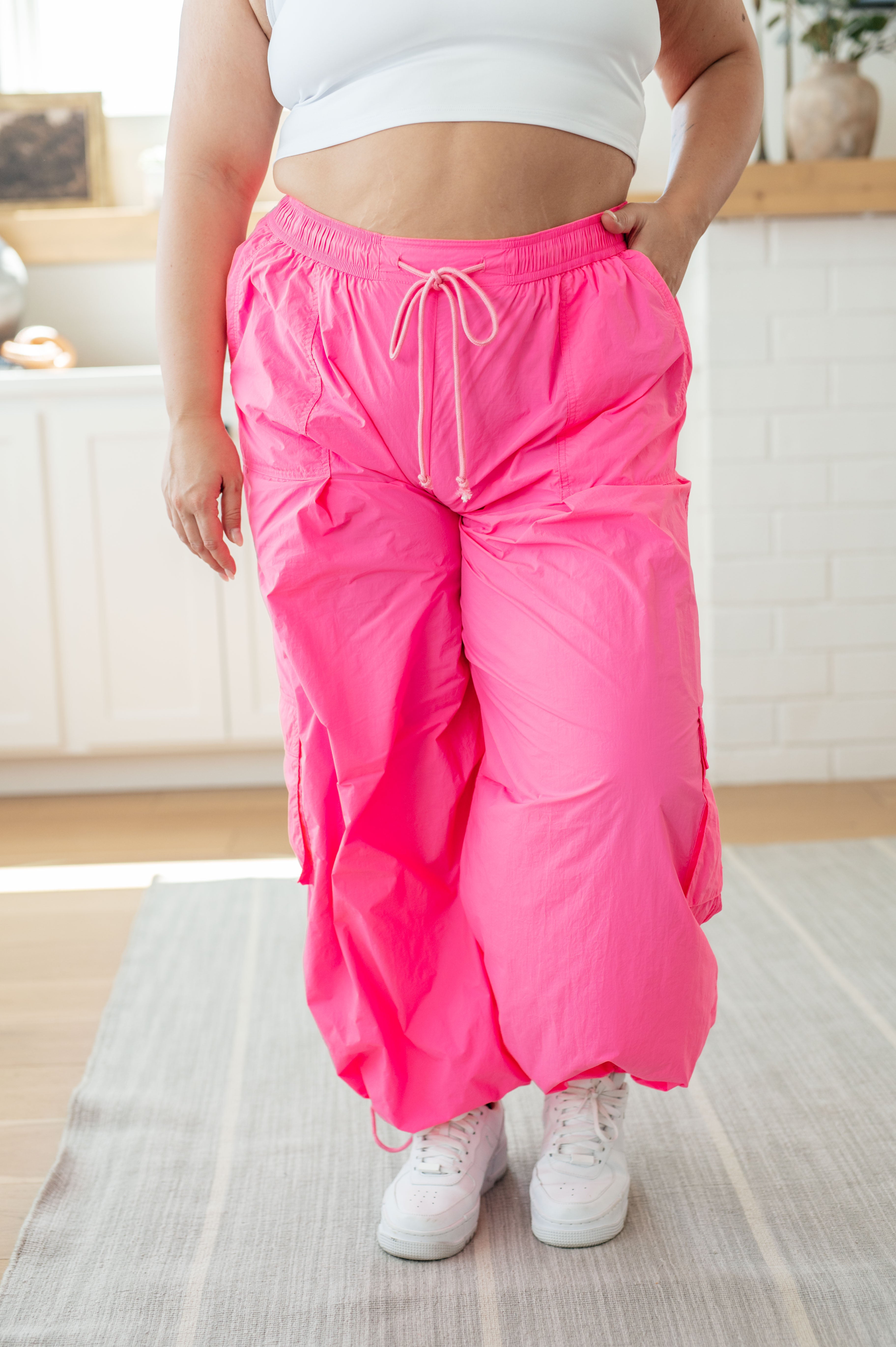 Front view of woman wearing bright fuchsia First Place Cargo Pants with drawstring waist and roomy pockets, styled with white sneakers in cozy indoor setting