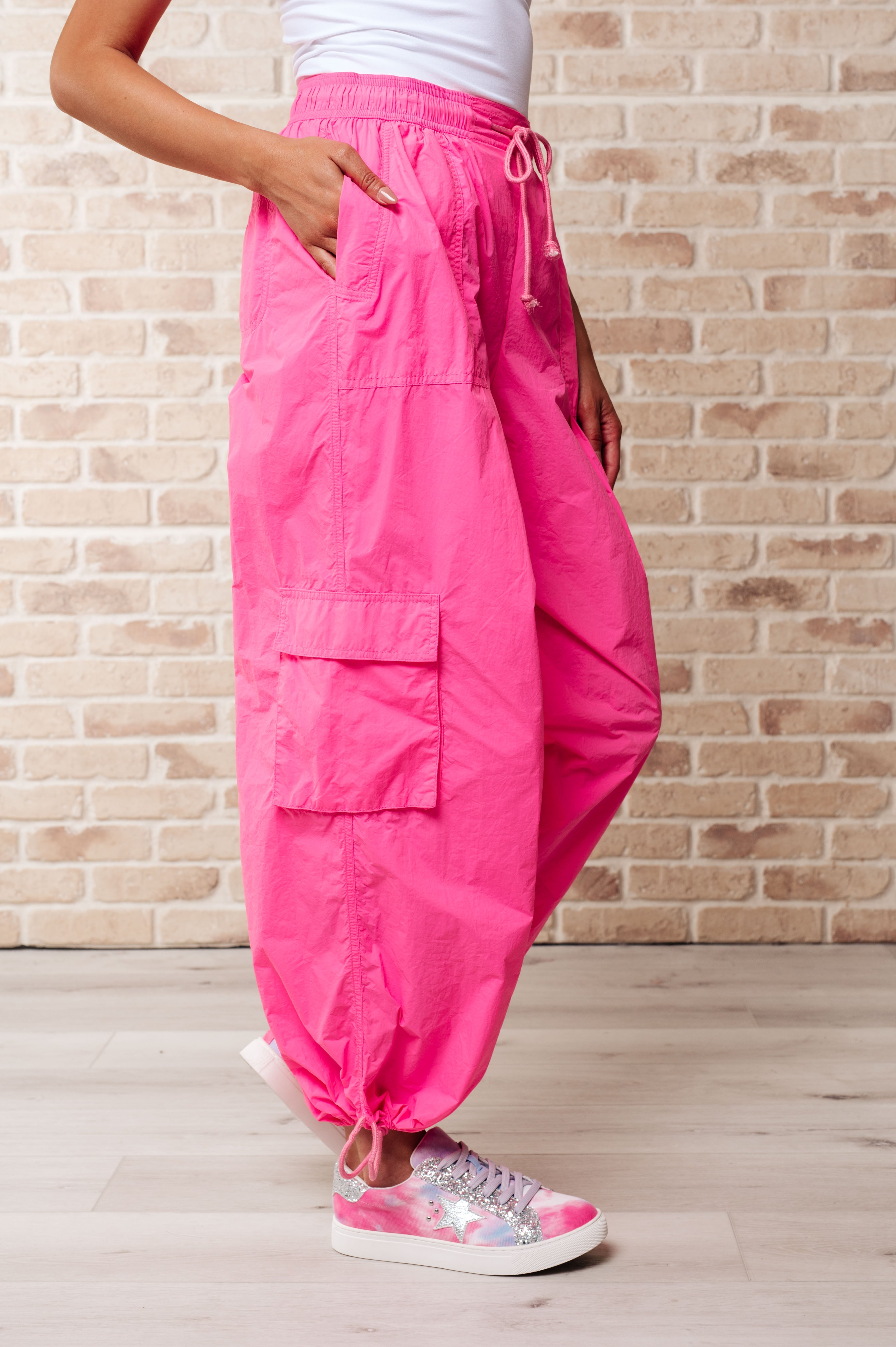 Side view of woman wearing bright fuchsia First Place Cargo Pants with drawstring waist and large side pocket, paired with colorful lace-up sneakers on light floor