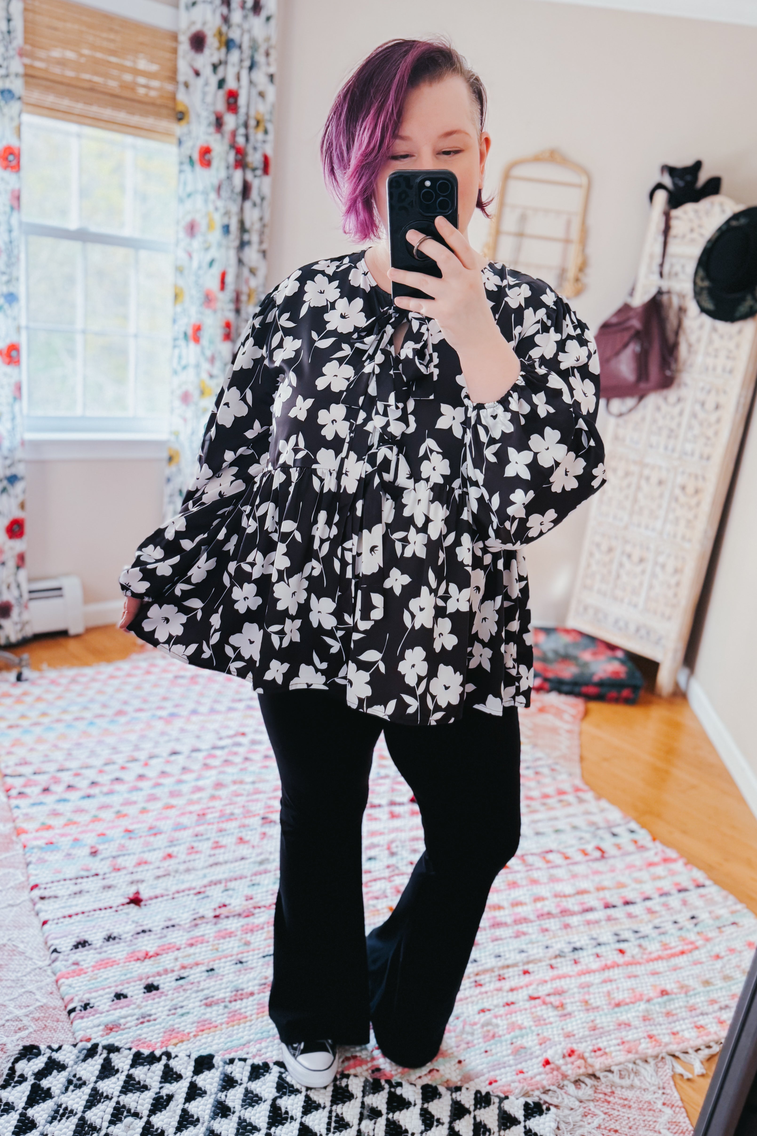 Fleur with Flair Double Bow Babydoll Top in black and white floral design, styled with black pants and sneakers in a bright, cozy room with patterned curtains.