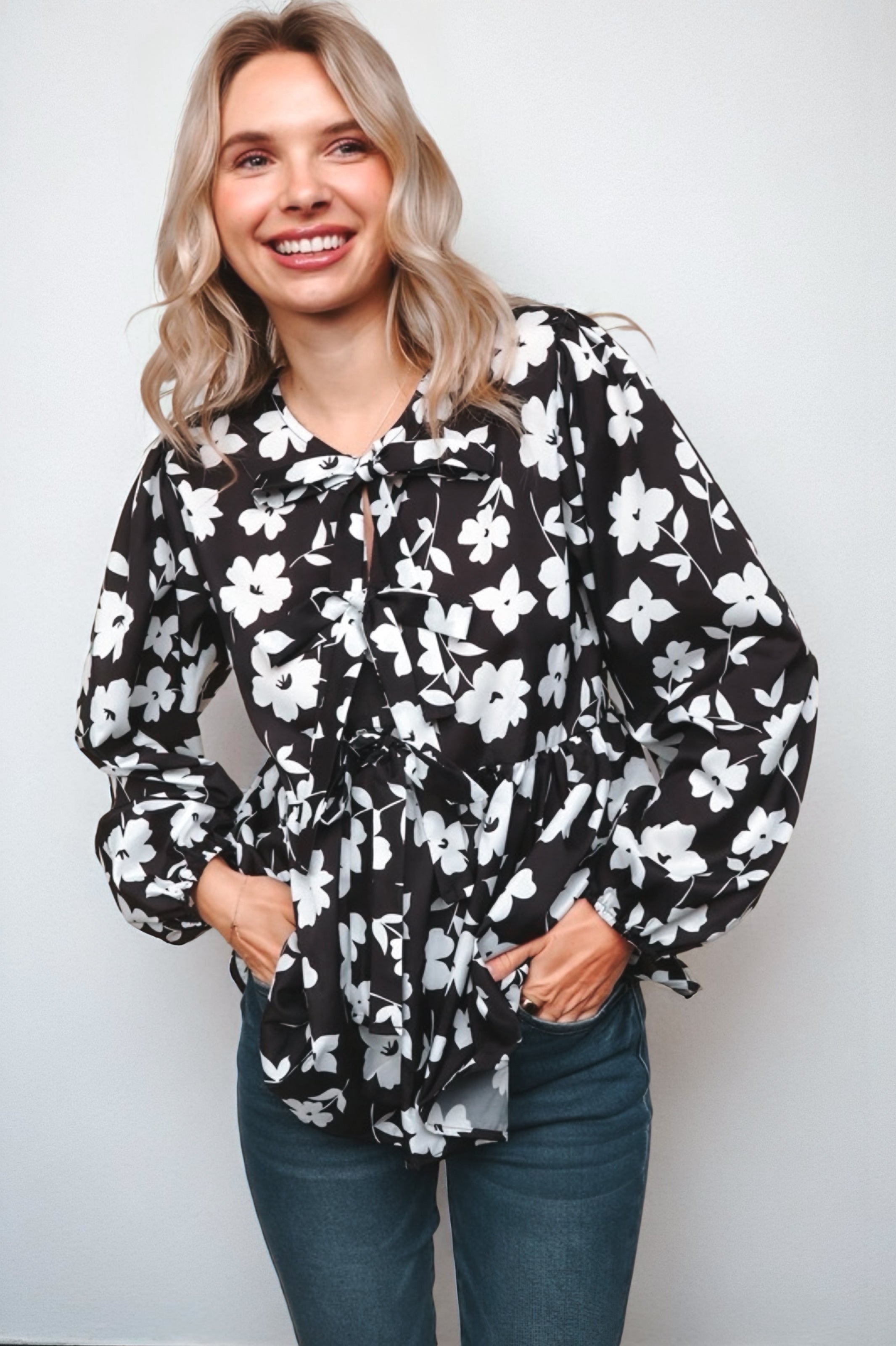 Fleur with Flair Double Bow Babydoll Top in black with bold white floral print, featuring puffed long sleeves and a tied bow neckline on a smiling woman.