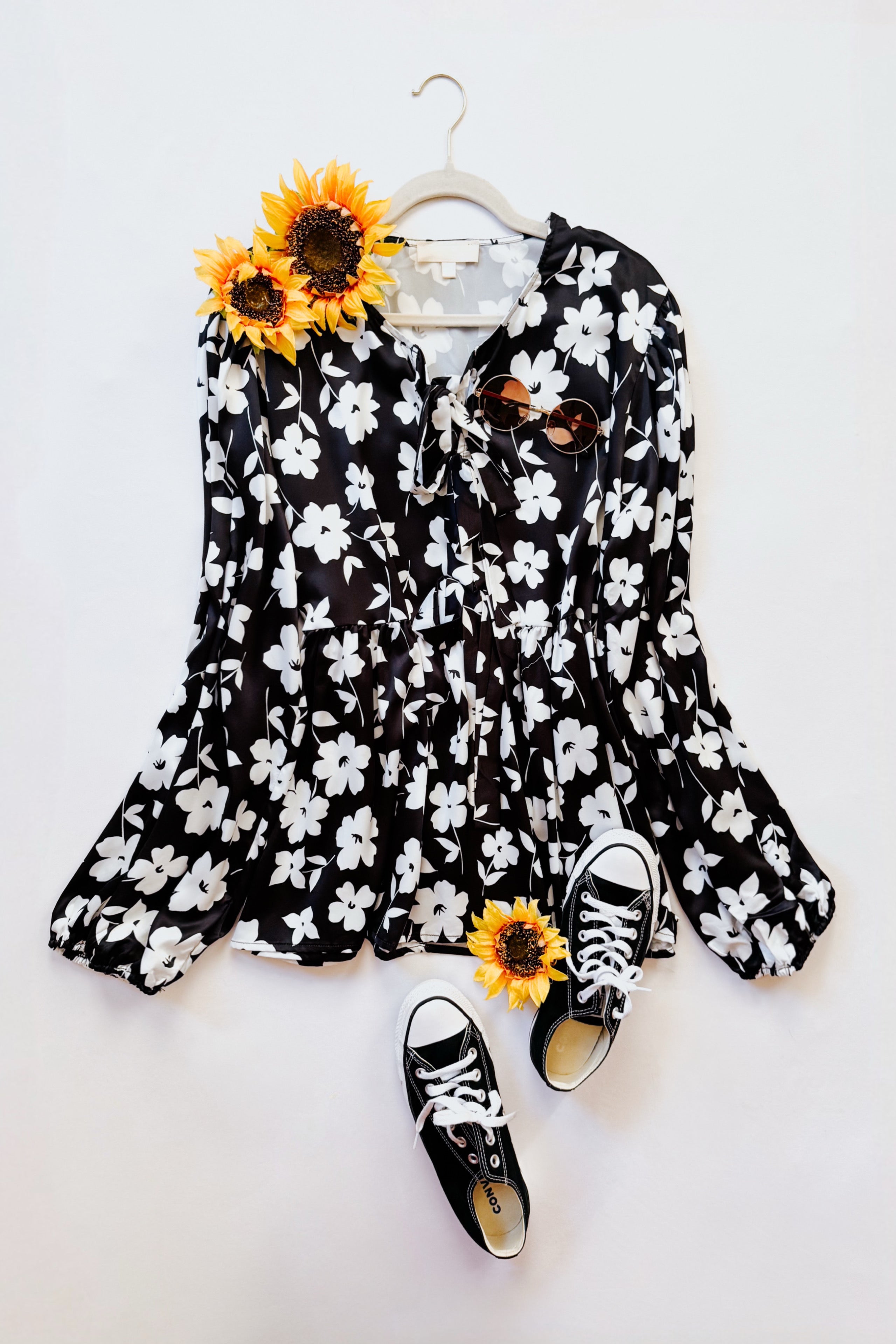 Fleur with Flair Double Bow Babydoll Top in black and white floral print styled with sunglasses and black canvas sneakers on a white background with sunflowers.