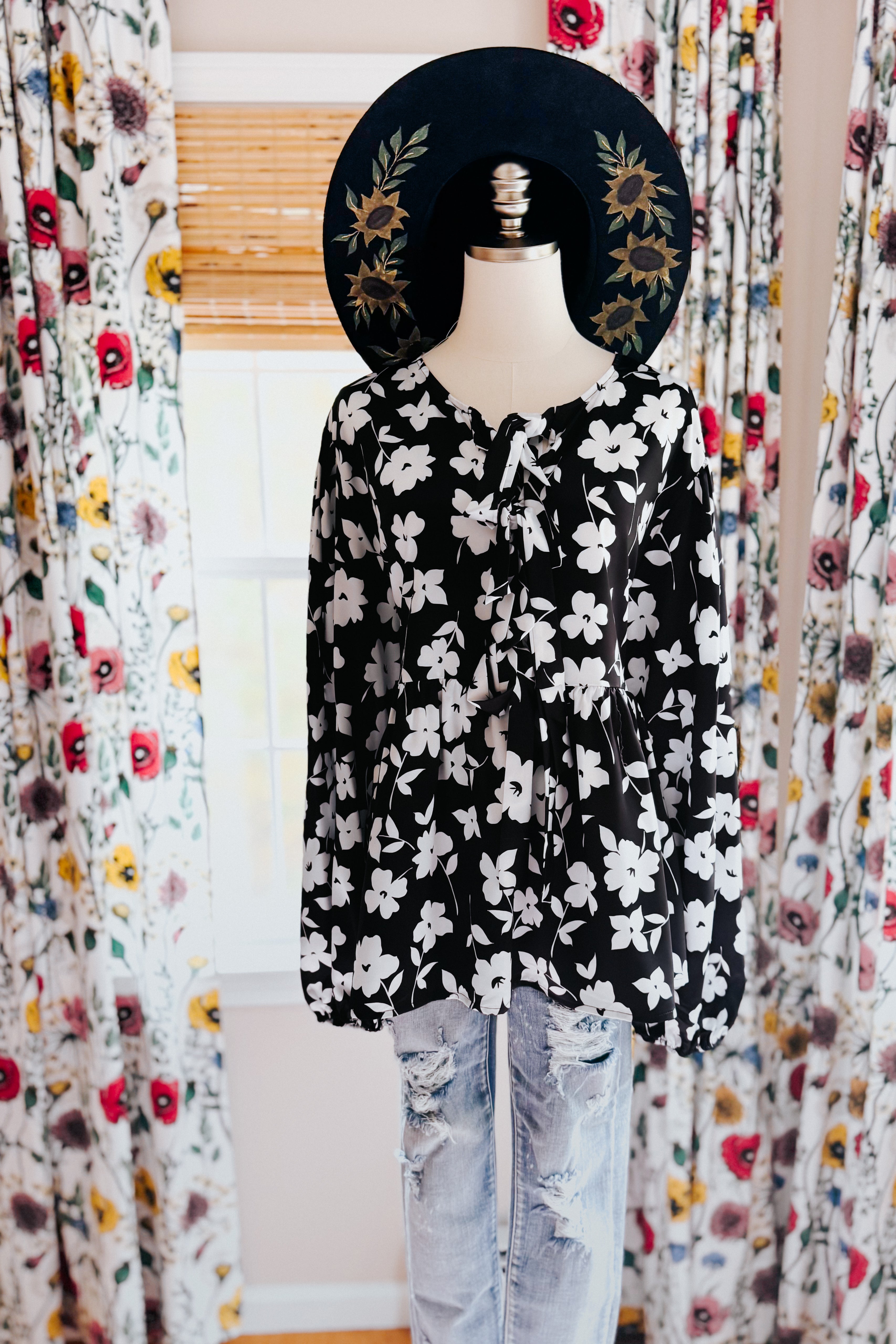 Fleur with Flair Double Bow Babydoll Top in black and white floral print styled on a mannequin with a sunflower hat and distressed light-wash jeans.