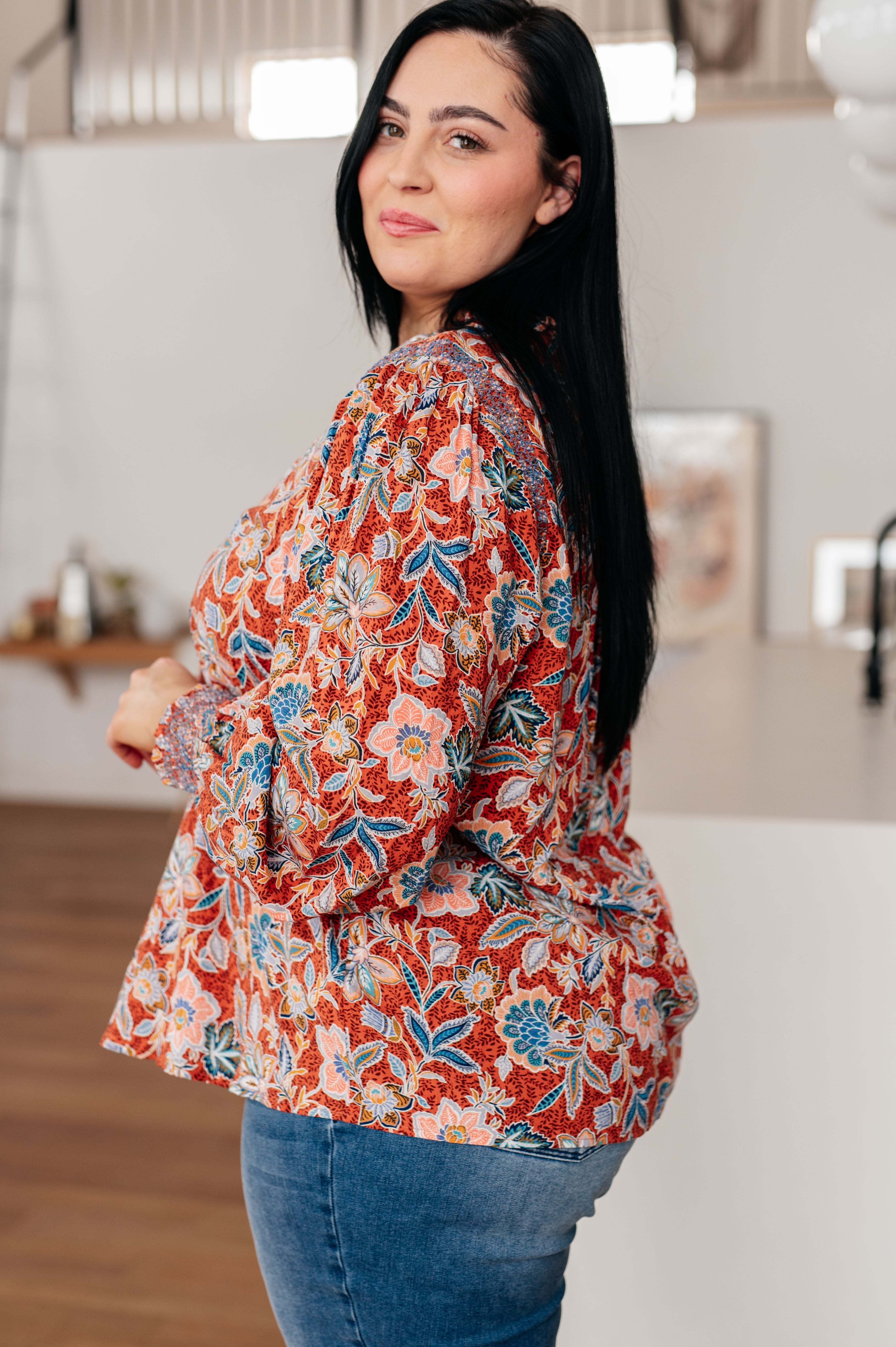 Woman wearing rust floral blouse with puff sleeves paired with blue jeans in cozy indoor setting