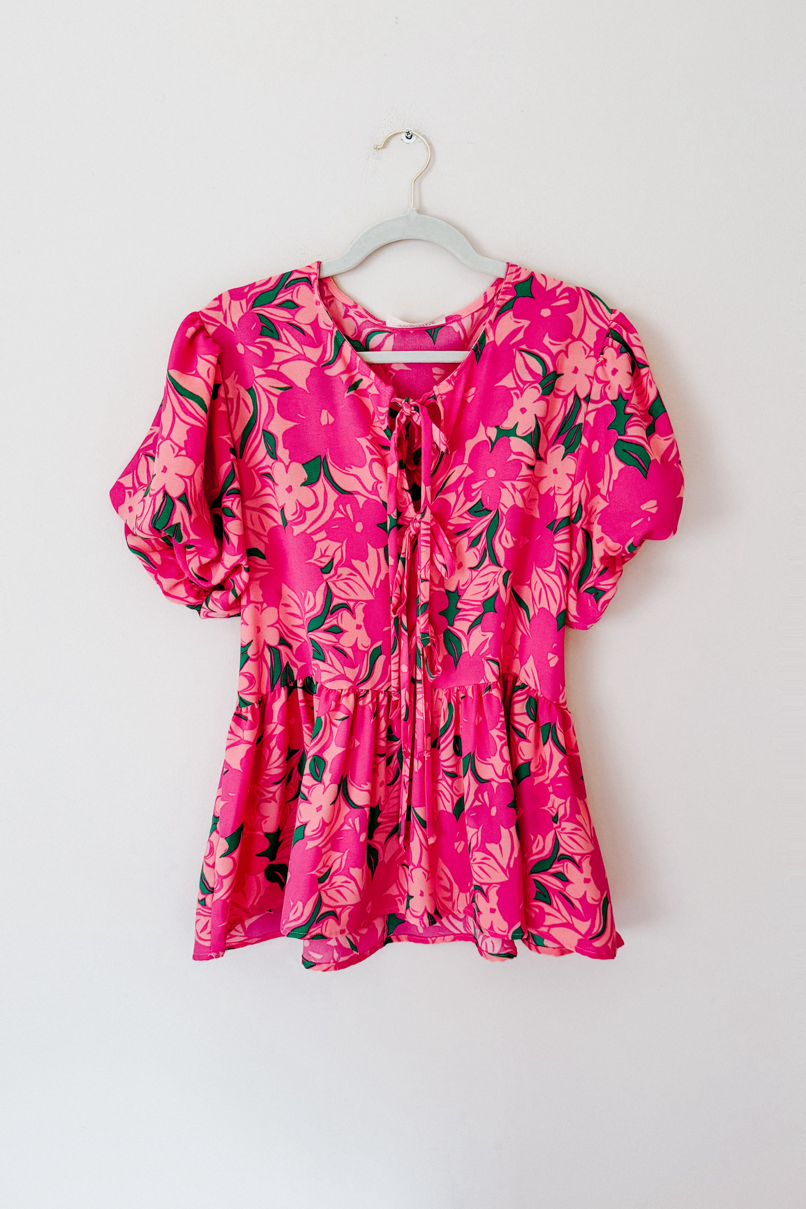 Floral Fling Puff Sleeve Blouse with vibrant pink floral print and tied neckline hanging against white background