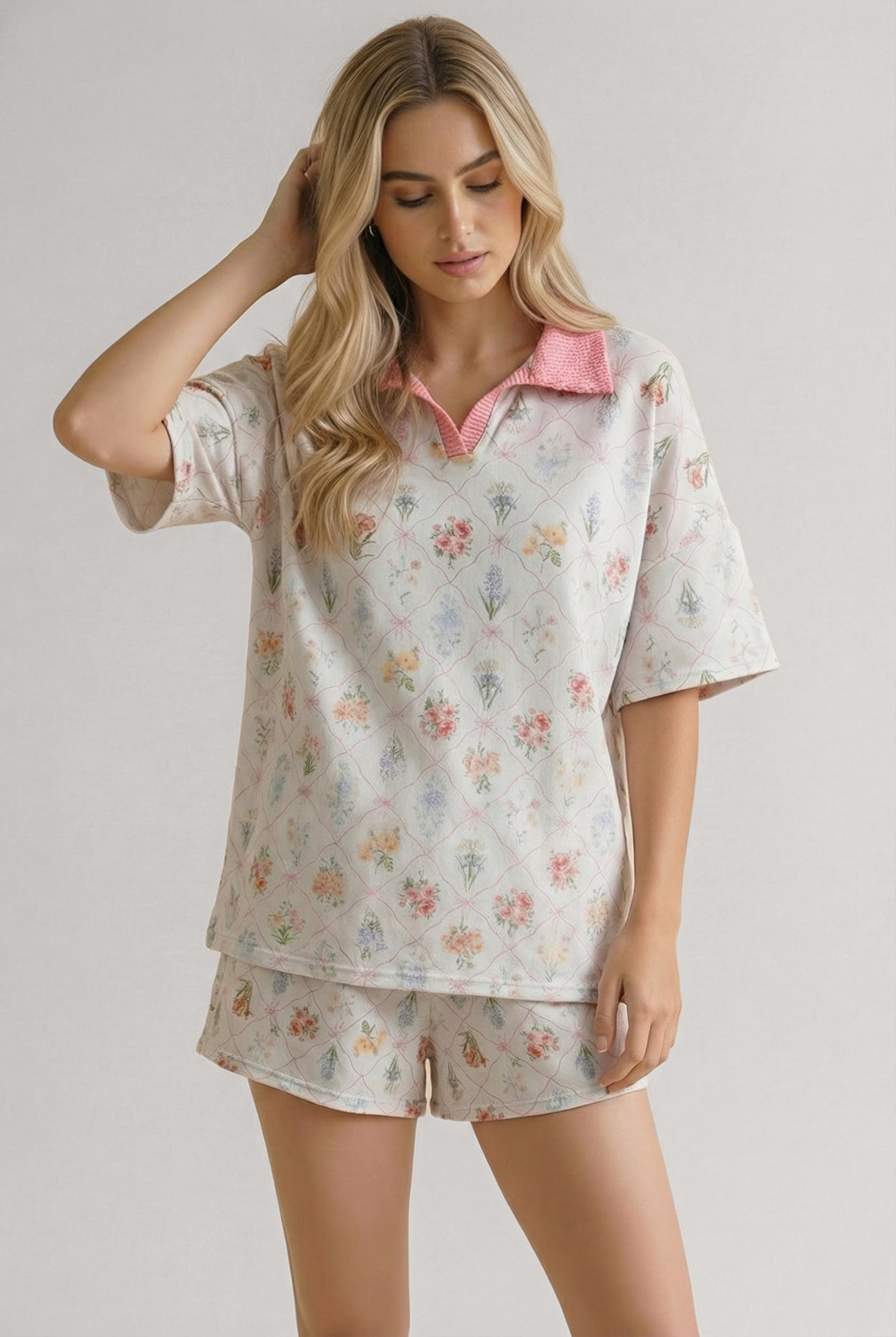 Woman wearing ivory floral garden matching short set with pink collar, standing with one hand touching hair