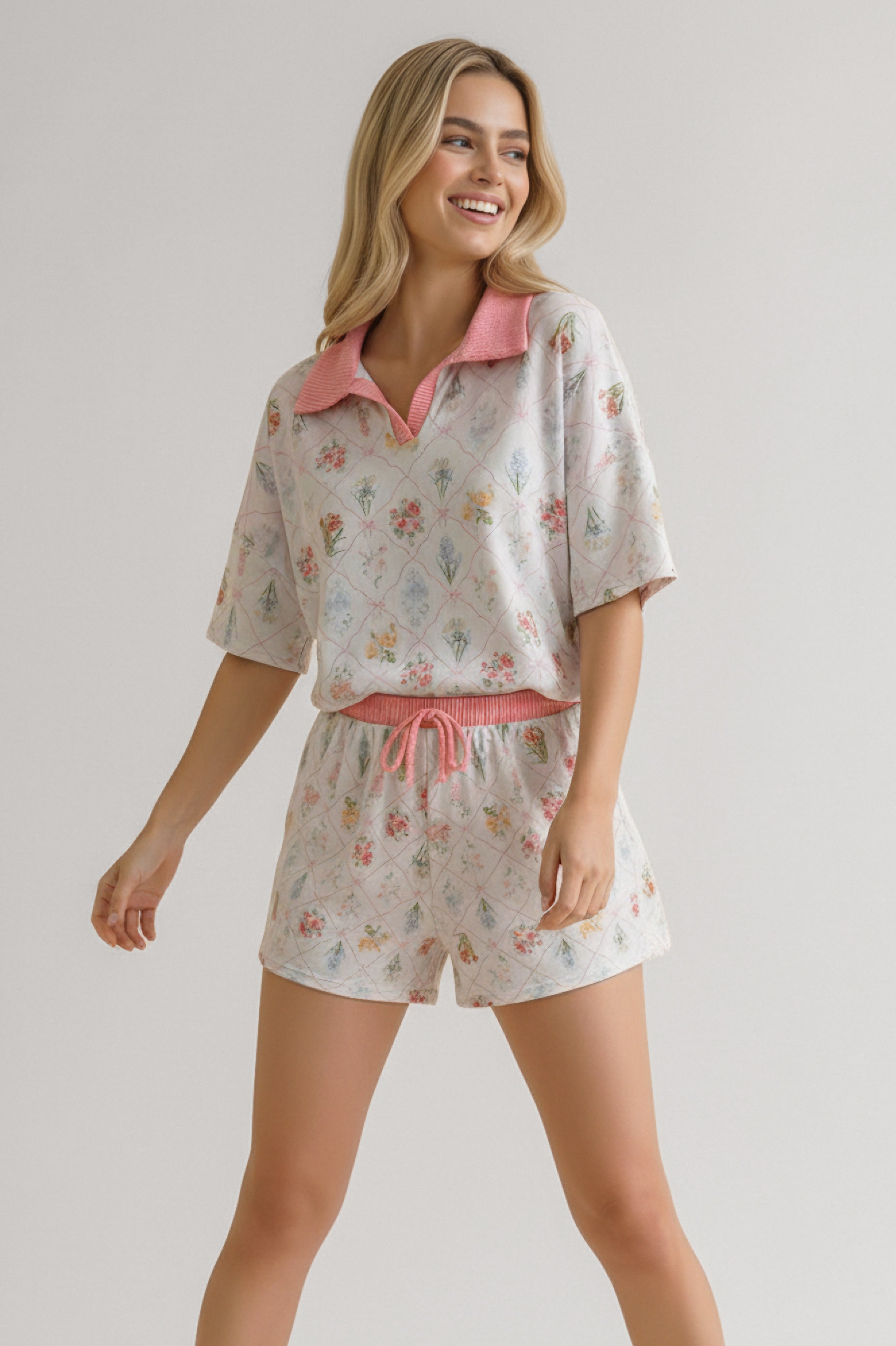 Smiling woman wearing ivory floral print short set with pink collar and waistband, posing with relaxed arms
