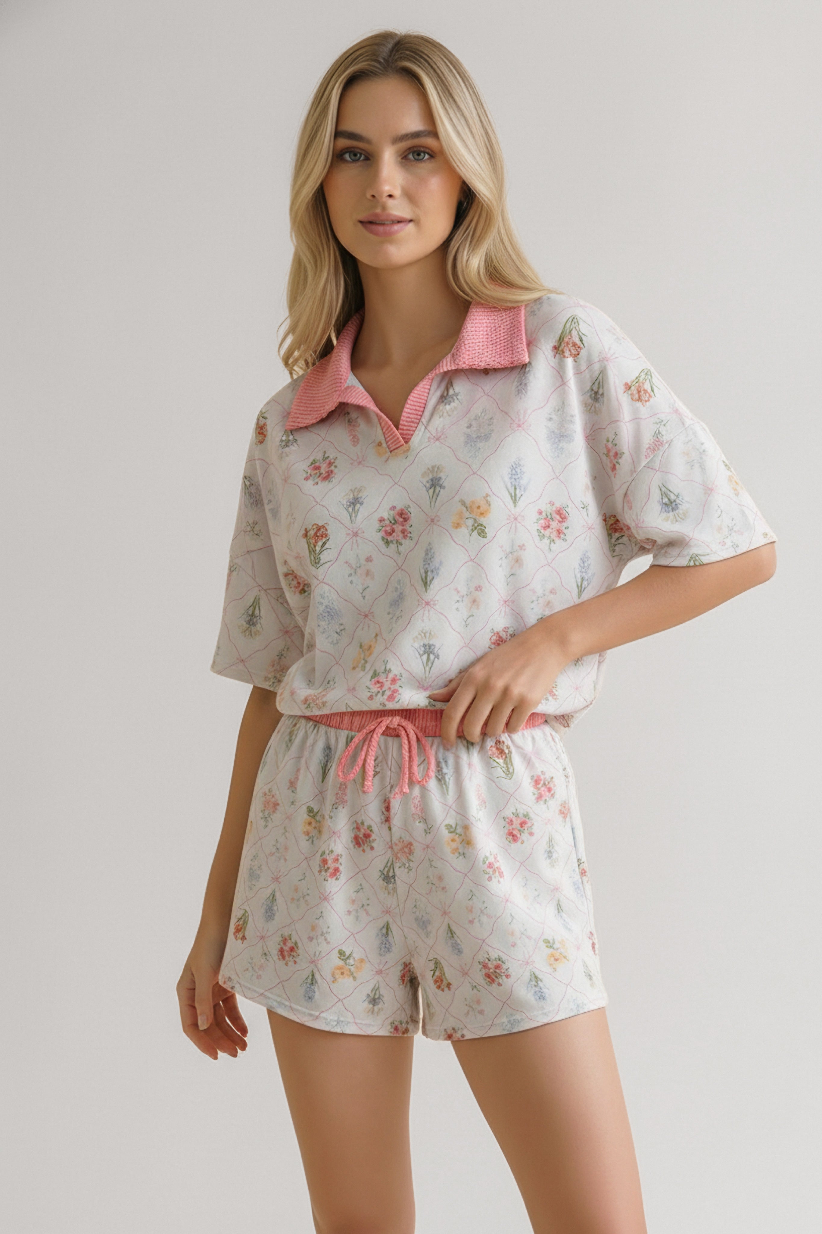 Woman wearing ivory floral garden matching short set with pink collar and drawstring posing with hand on waist