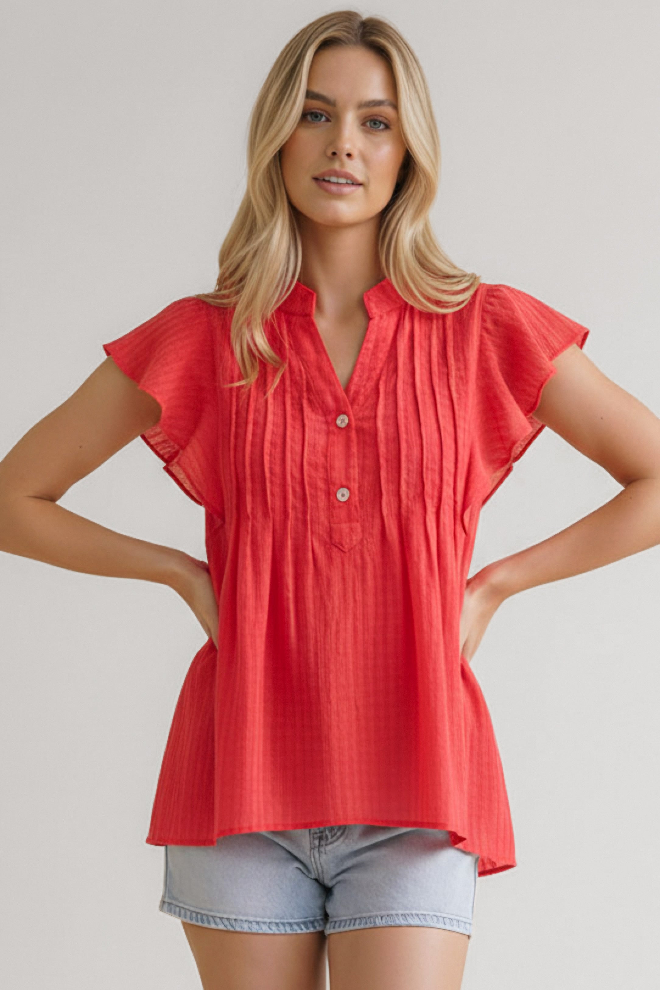 Woman wearing coral textured blouse with flutter sleeves and button front paired with light denim shorts