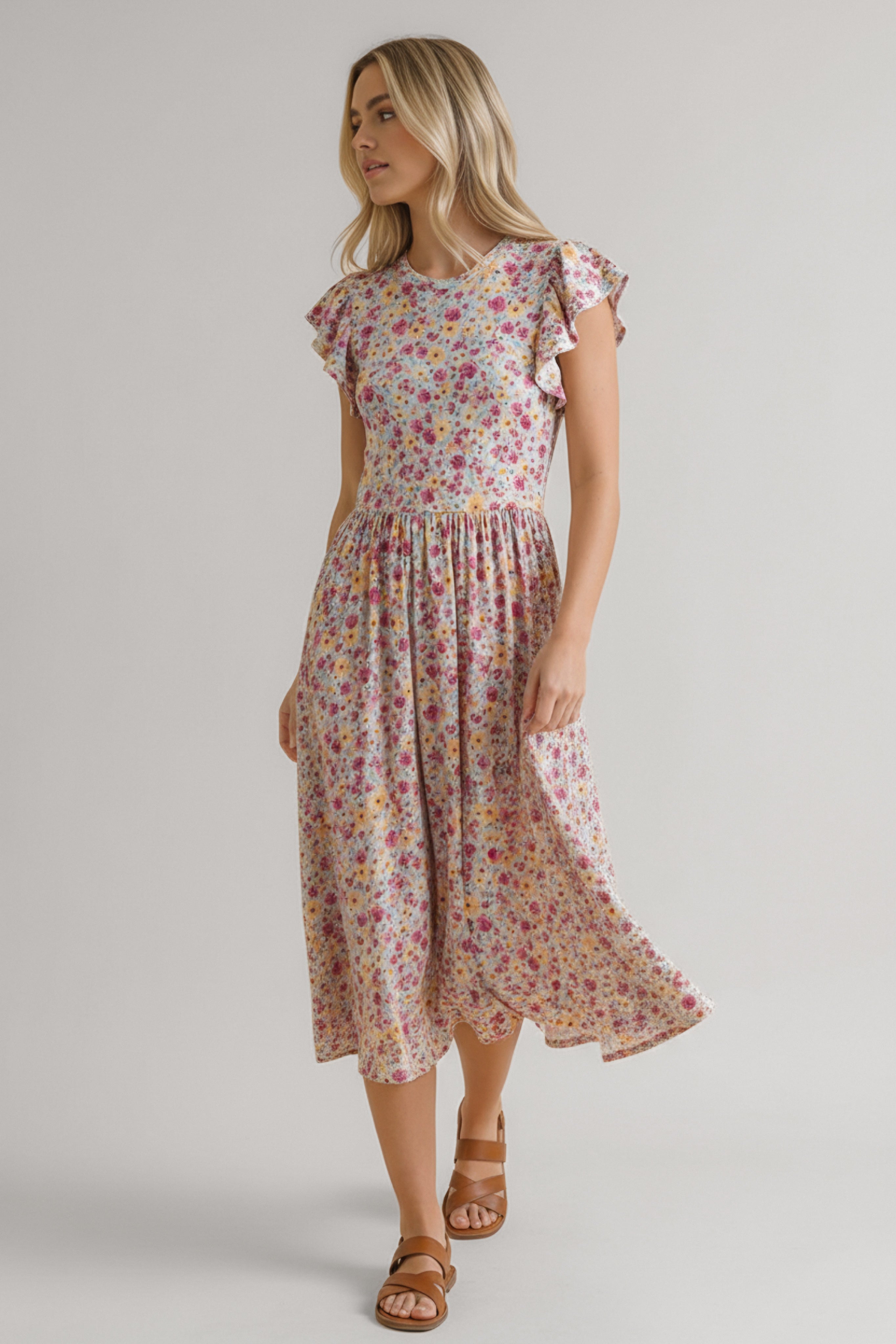 Woman in a pink floral midi dress with flutter sleeves and a gathered waist paired with brown sandals